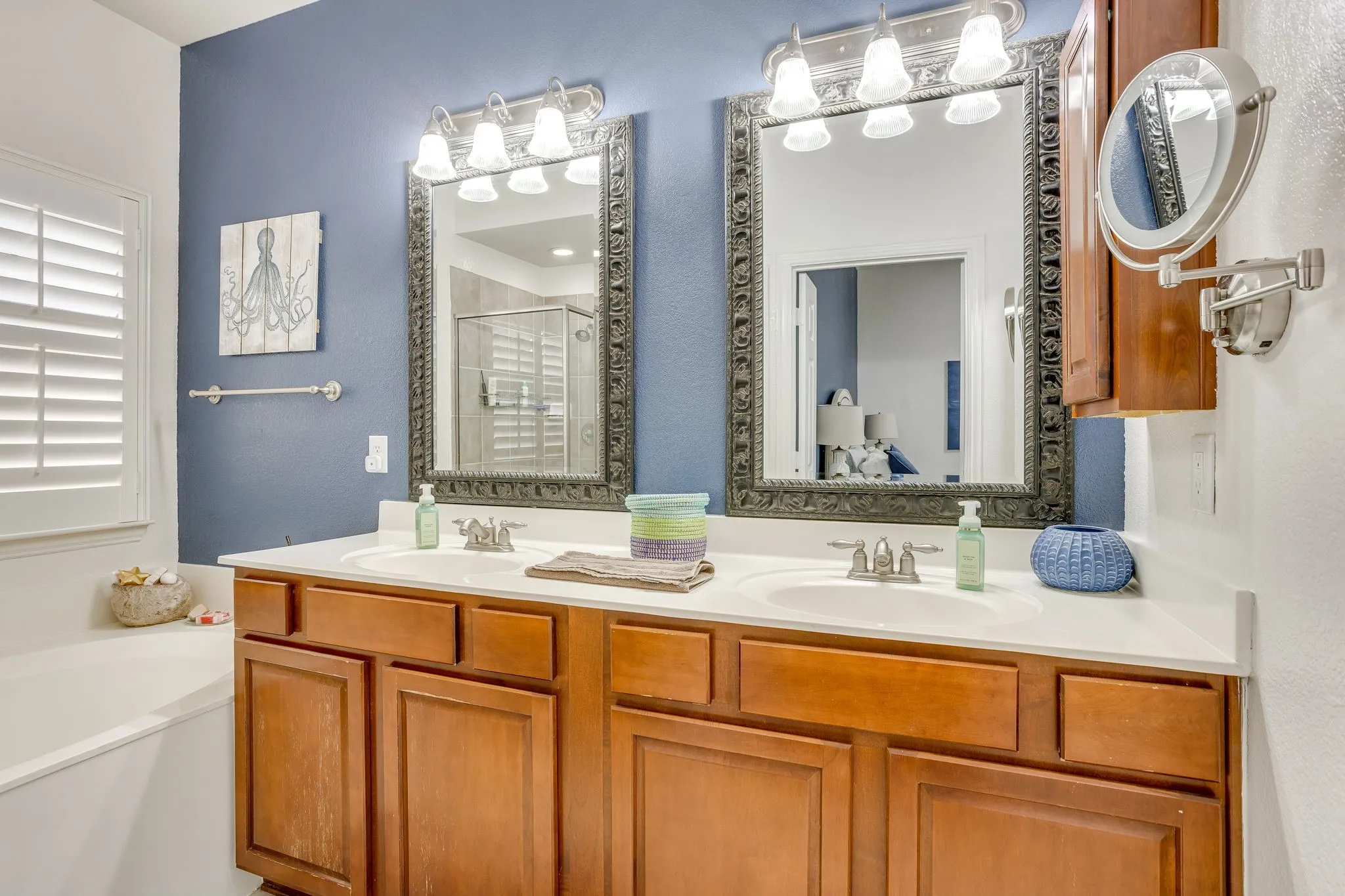 Dual vanity with light-toned countertop and wood-finish cabinetry, featuring two decorative framed mirrors, each with a three-light vanity fixture