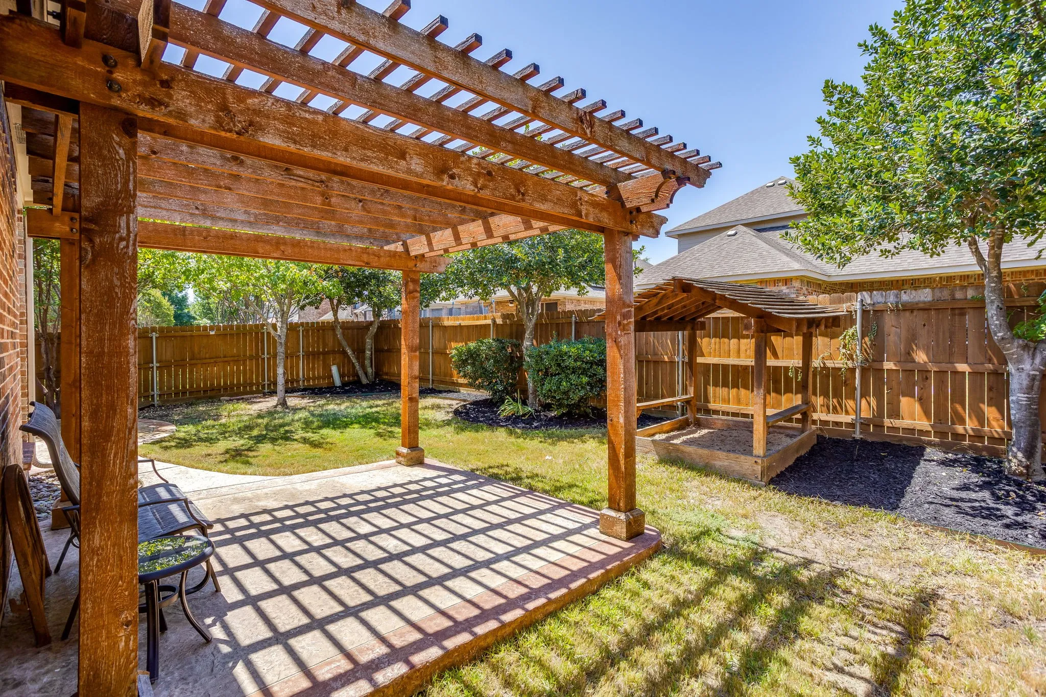 Expansive backyard featuring a wood pergola, concrete patio, privacy fencing, and mature trees
