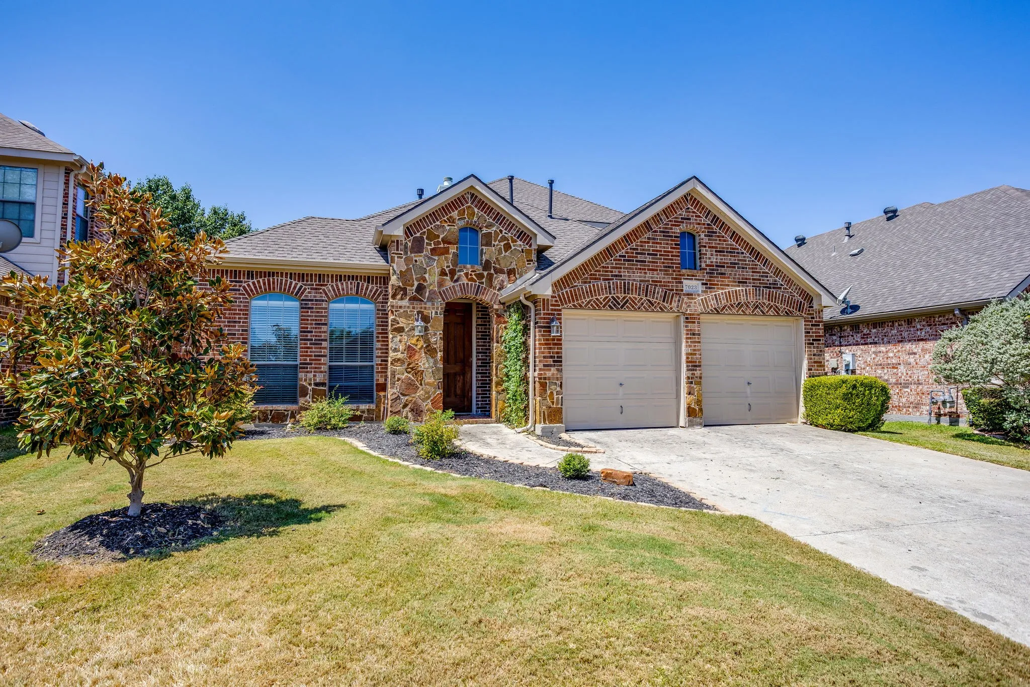 Brick and stone facade with arched windows, a two-car garage, and a concrete driveway