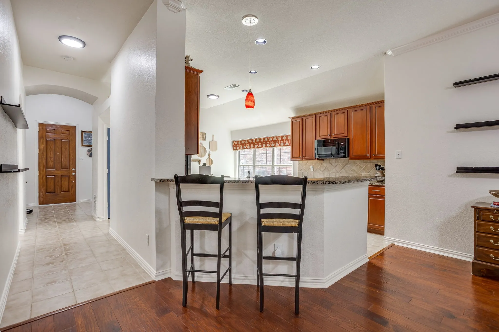 Wood-finish flooring, tiled entryway, kitchen with wood cabinetry, integrated microwave, and a breakfast bar with a stone-finish countertop