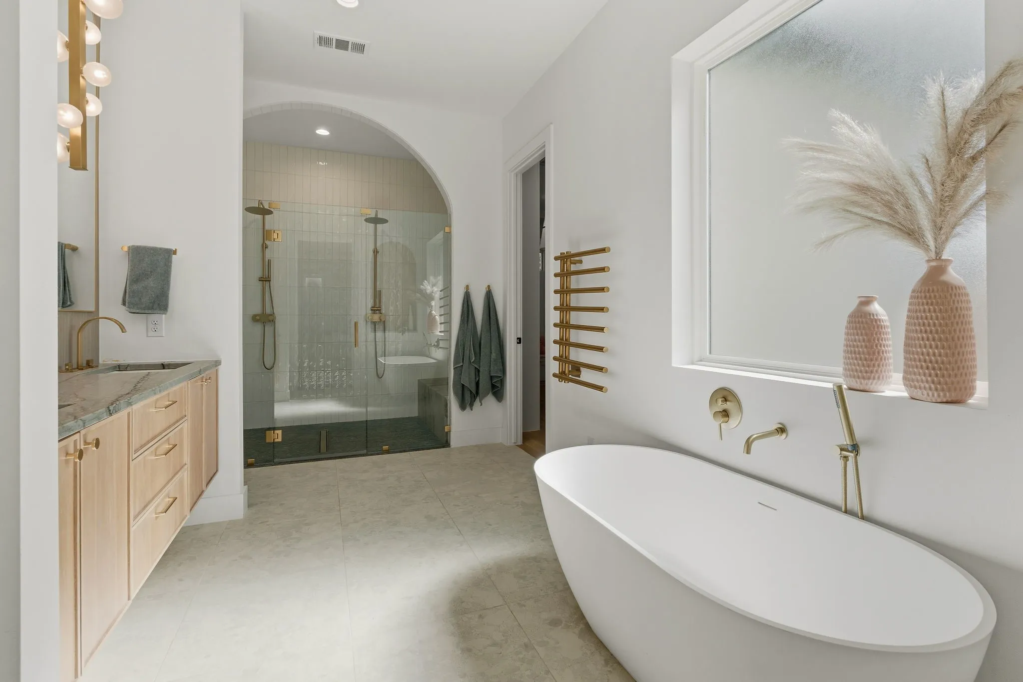 Freestanding soaking tub, walk-in shower with dual shower heads, wood-finish vanity with stone countertop, and light-toned tile flooring