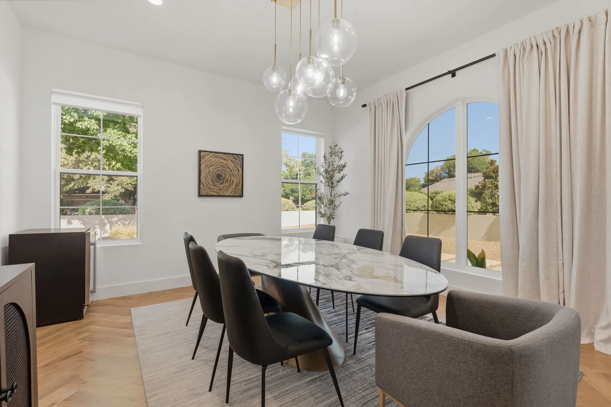 Spacious room featuring multiple windows, a prominent arched window, wood-finish herringbone flooring, and a contemporary chandelier