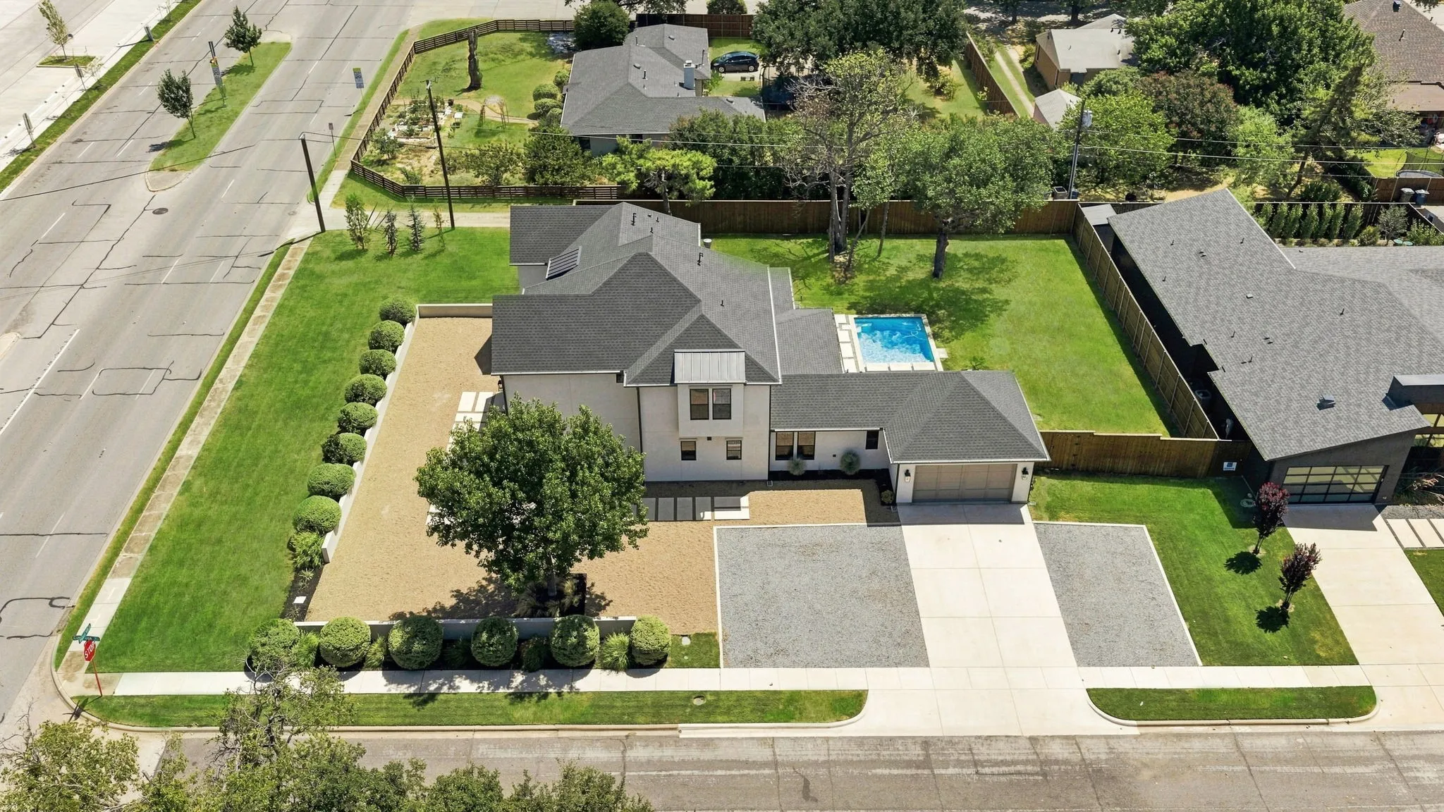 Exterior featuring a light-colored facade, dark shingle roof, attached garage, private swimming pool, and extensive paved and landscaped areas