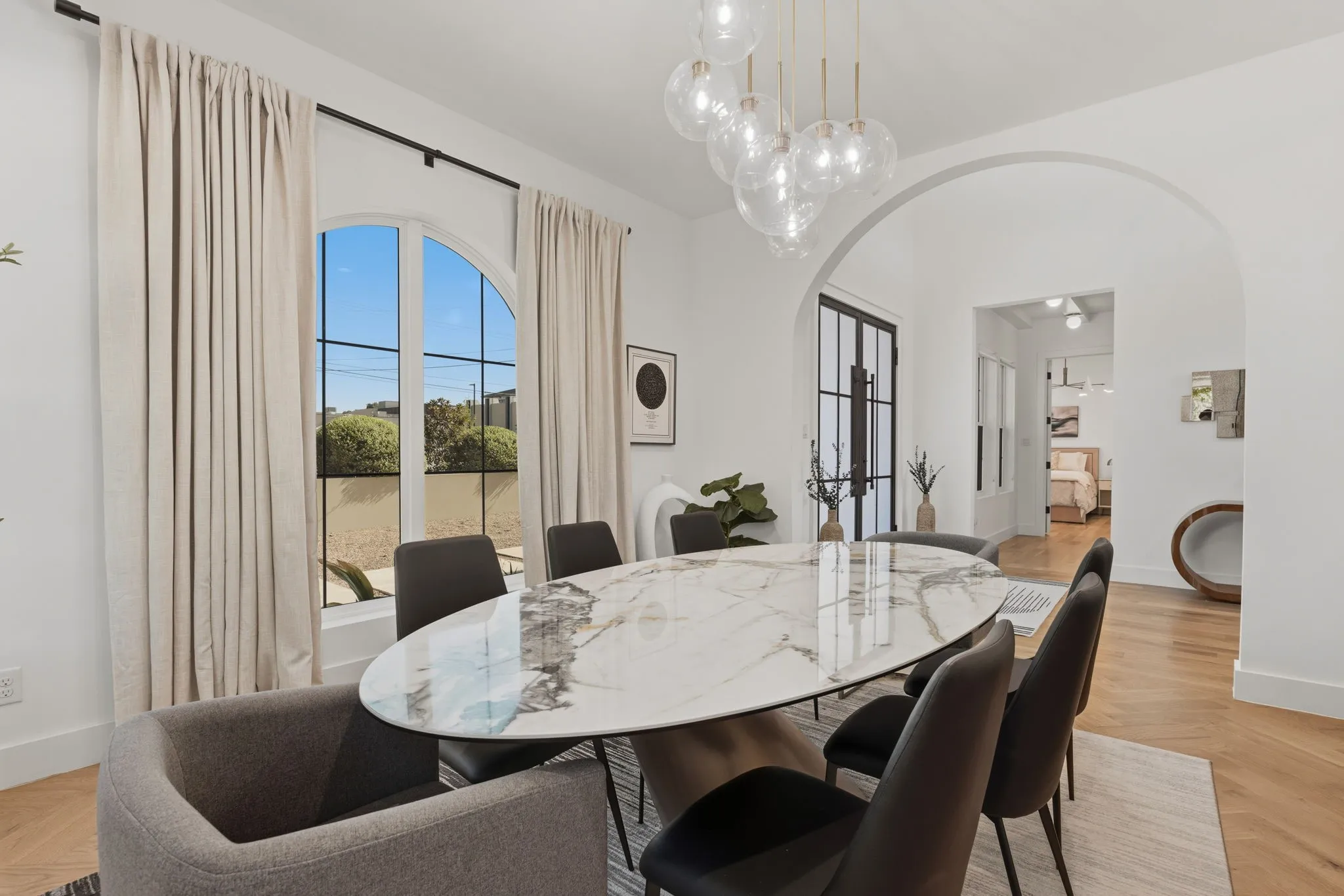 Arched window, high ceilings, arched entryways, wood-finish flooring, and a modern chandelier