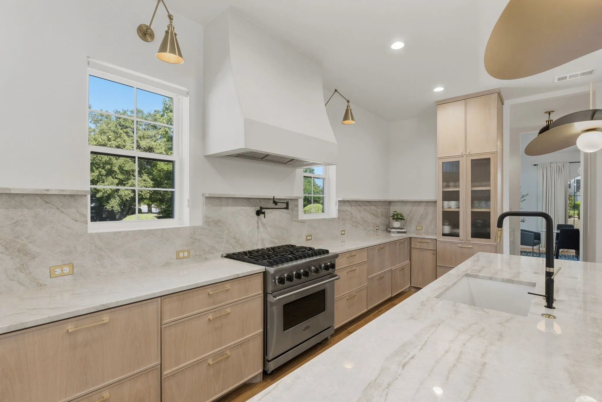 Gourmet kitchen featuring a built-in stainless steel range, white range hood, light-toned wood cabinetry, and extensive light-toned countertops with matching backsplash