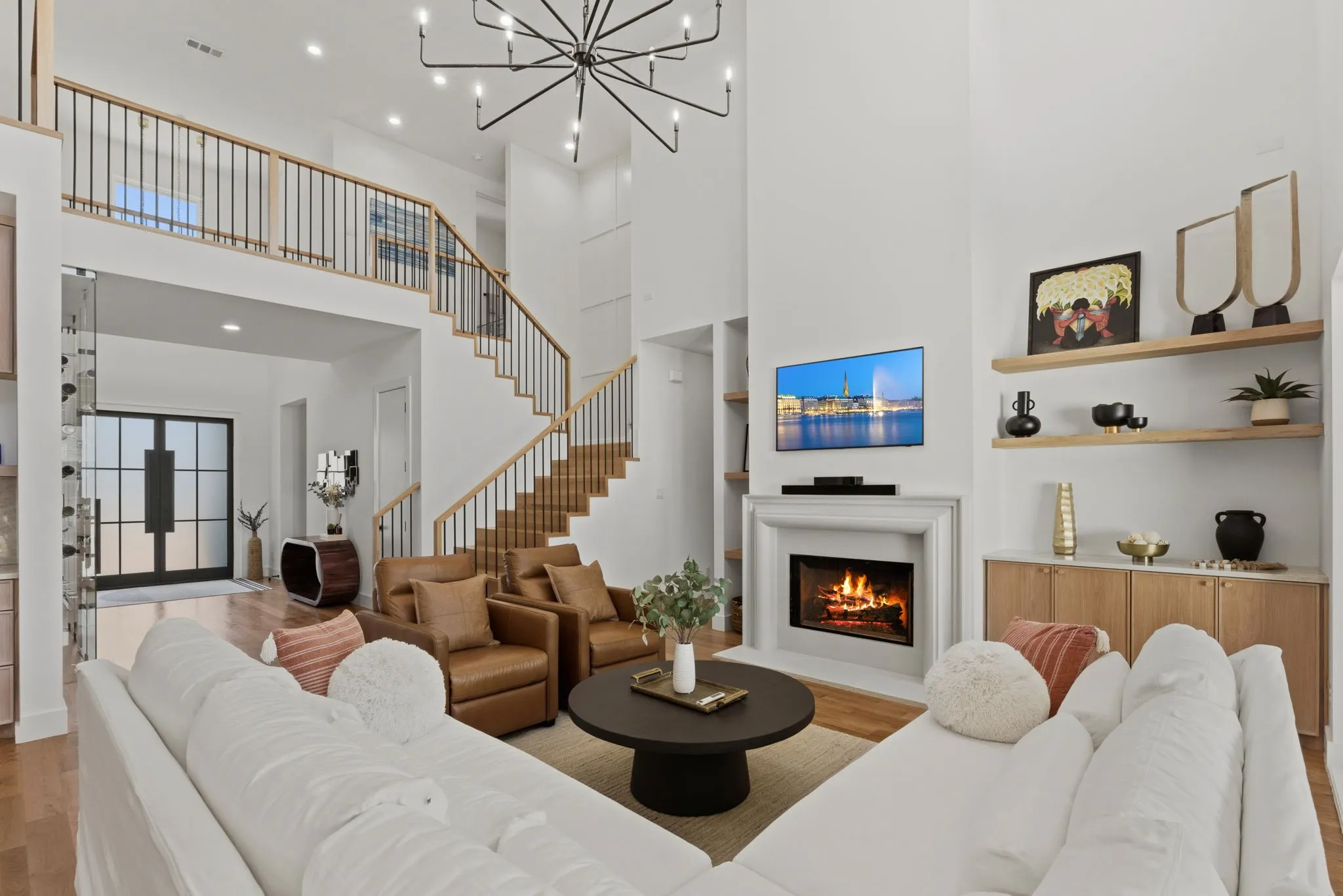 Two-story living area with high ceilings, a grand staircase with wood and metal railings, and a prominent fireplace with a substantial mantel