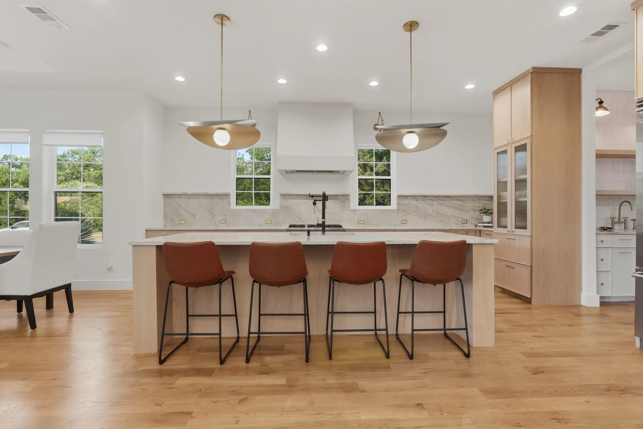 Expansive kitchen island with seating, pendant lighting, hardwood flooring, and light wood-finish cabinetry