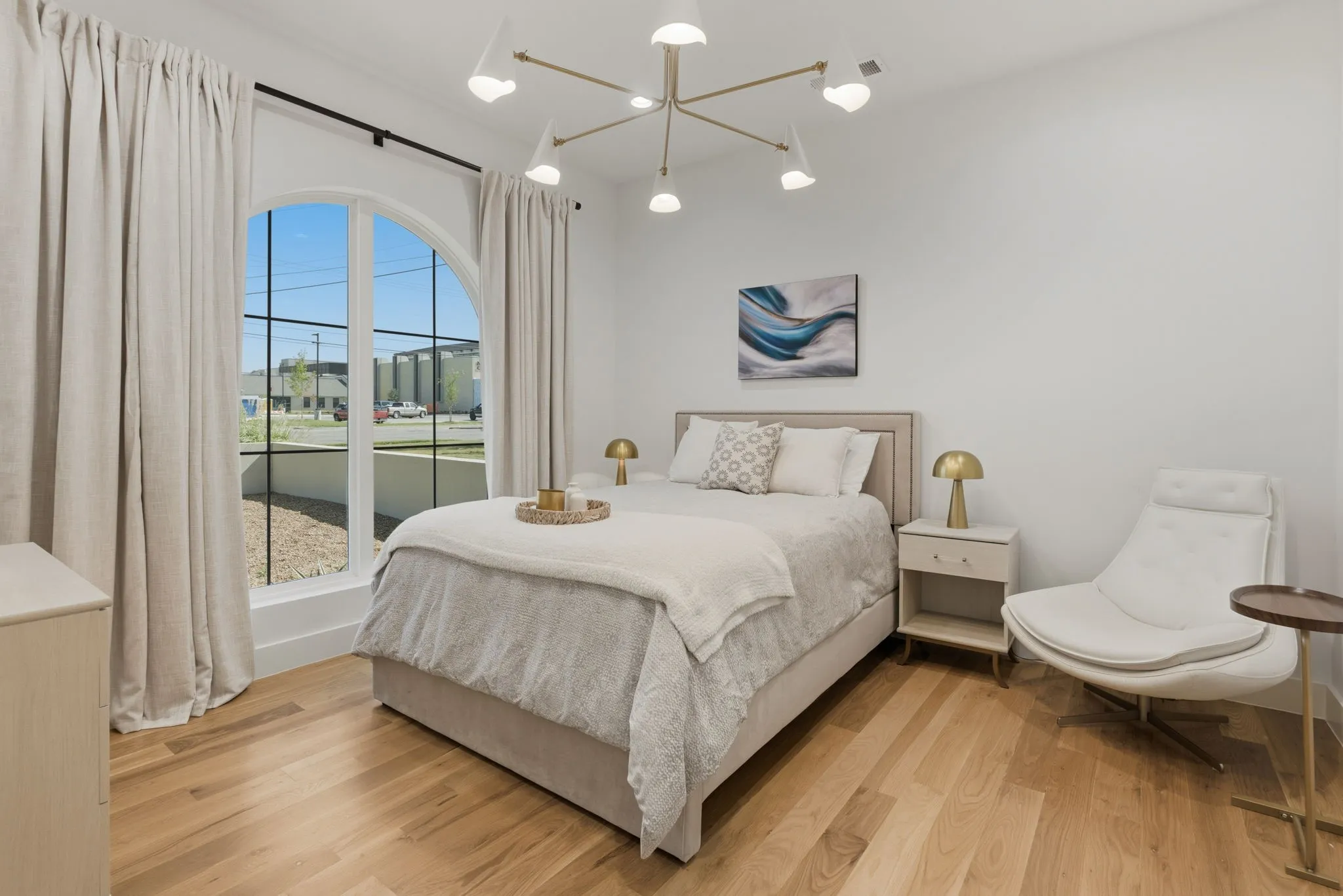 Arched window with black grid detail, light wood-finish flooring, white walls, and a modern ceiling light fixture