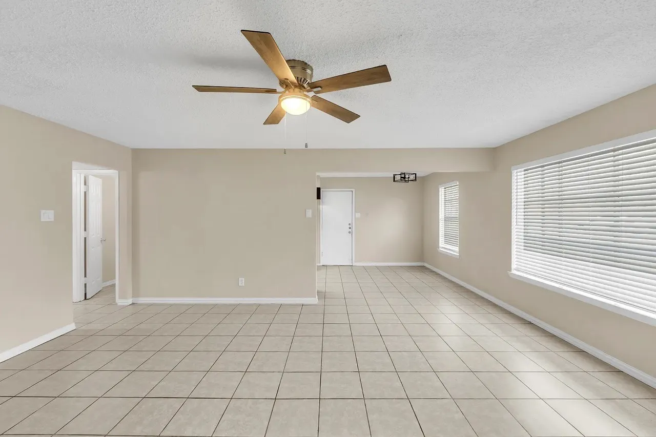 Spacious room featuring neutral-toned walls, square tile flooring, and a ceiling fan