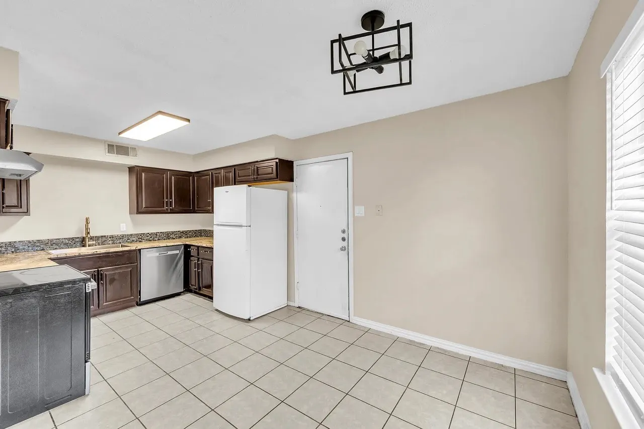 Kitchen featuring dark wood-finish cabinetry, granite-style countertops, stainless steel dishwasher, tile flooring, and a modern ceiling fixture