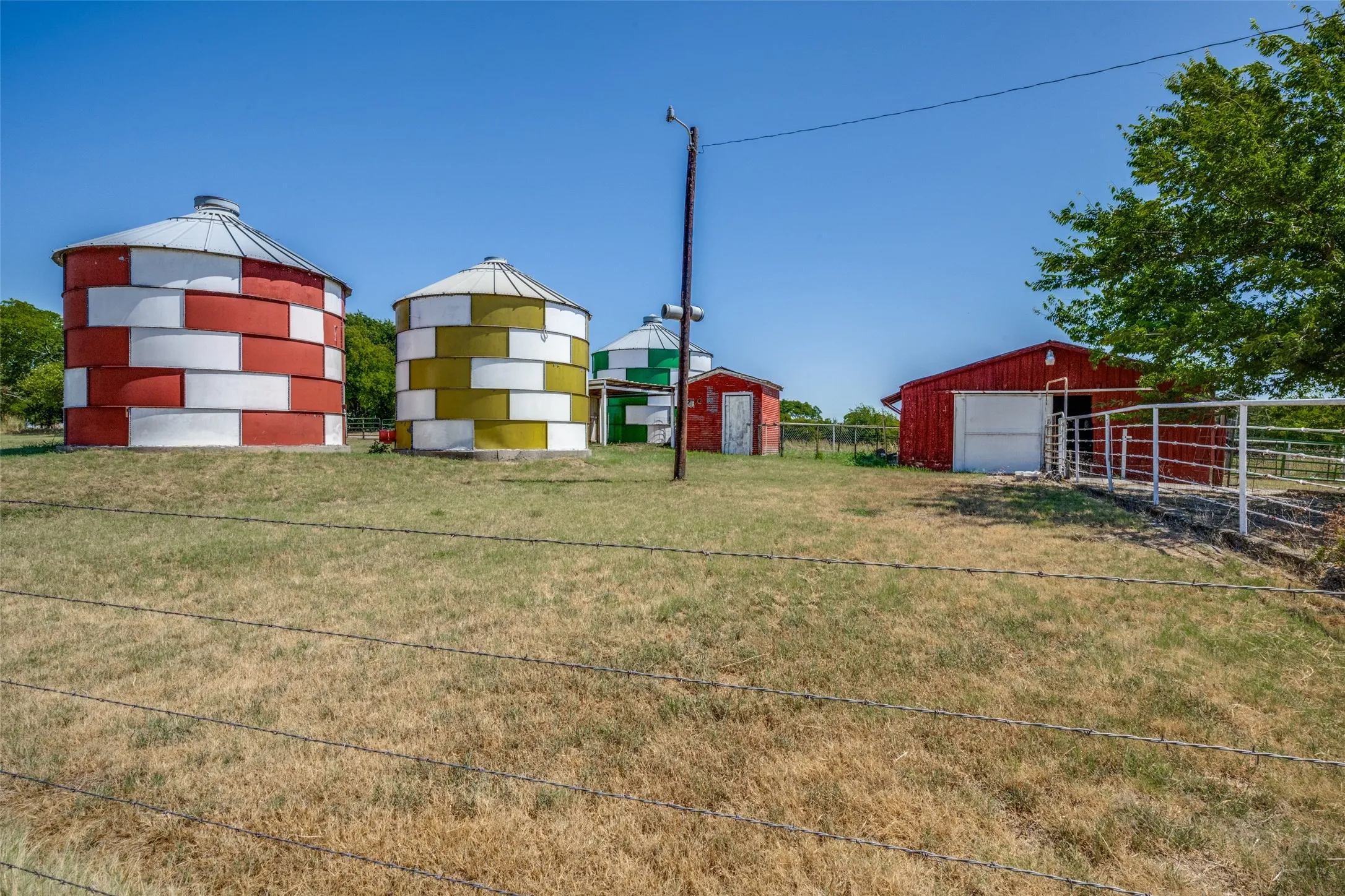 Three colorful silos, red barn structure, and metal fencing