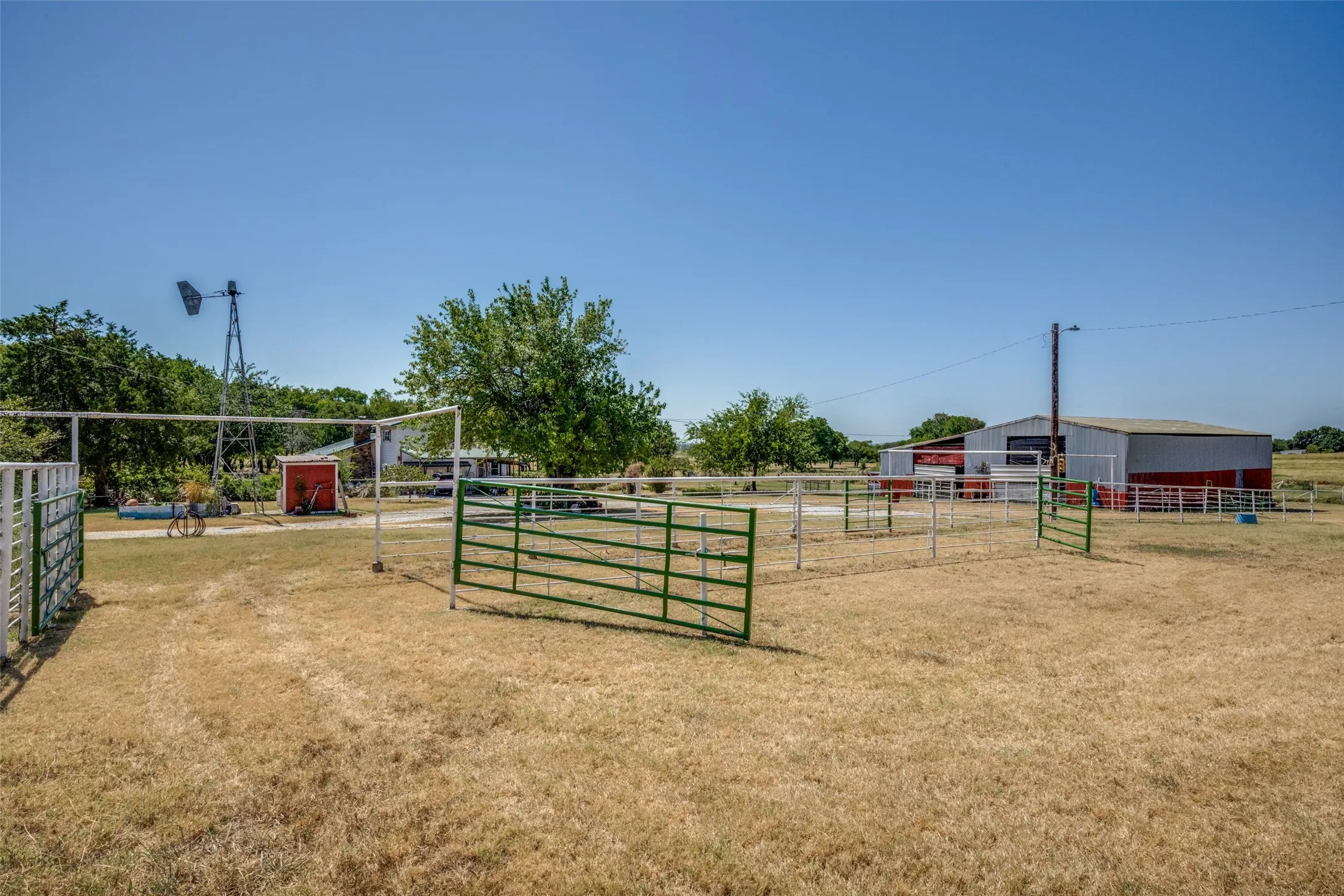 Expansive outdoor area featuring multiple metal fence enclosures, a metal barn structure with red trim, and a prominent windmill