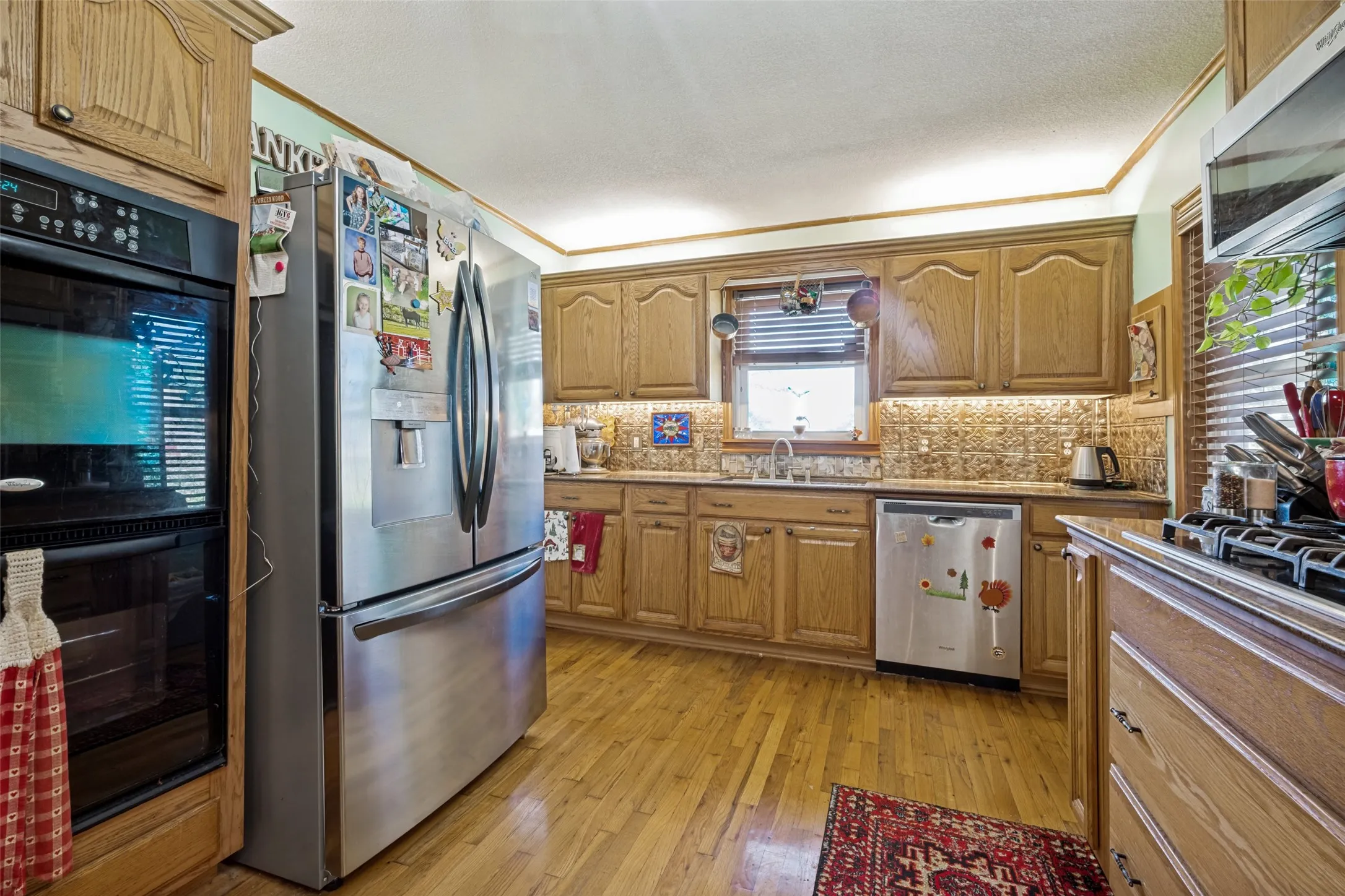 Kitchen featuring wood cabinetry, stainless steel appliances, a tile backsplash, and wood-finish flooring