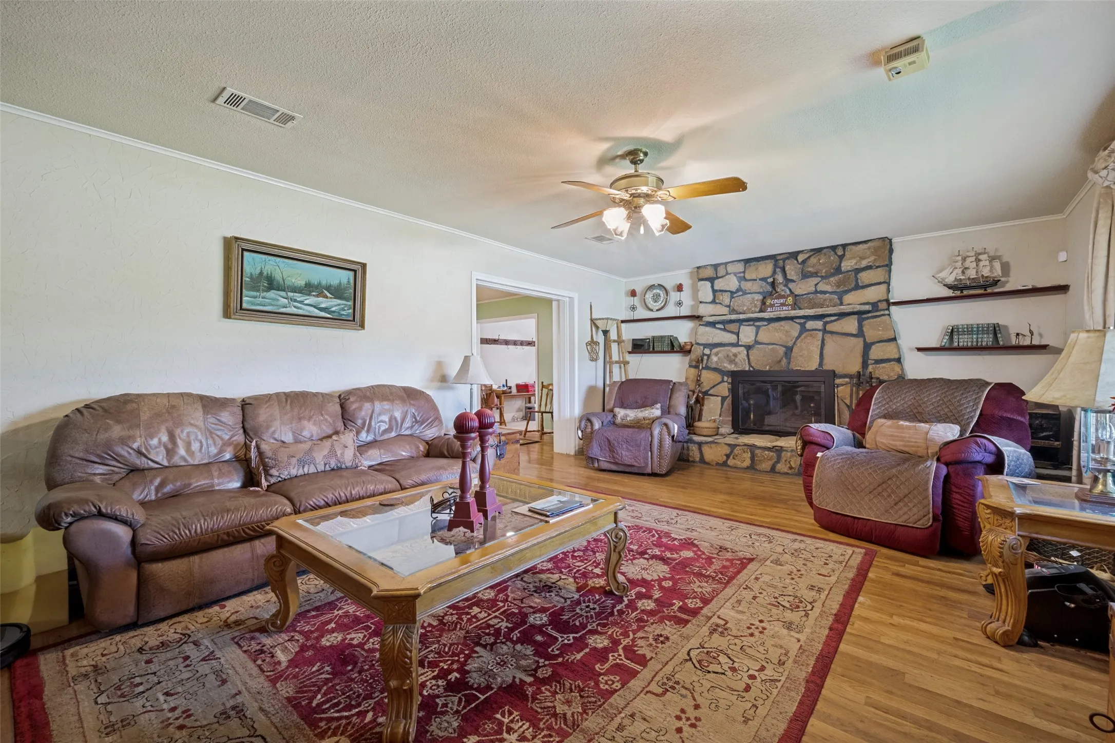 Stone fireplace with wood mantel, built-in shelving, wood-finish flooring, and a ceiling fan