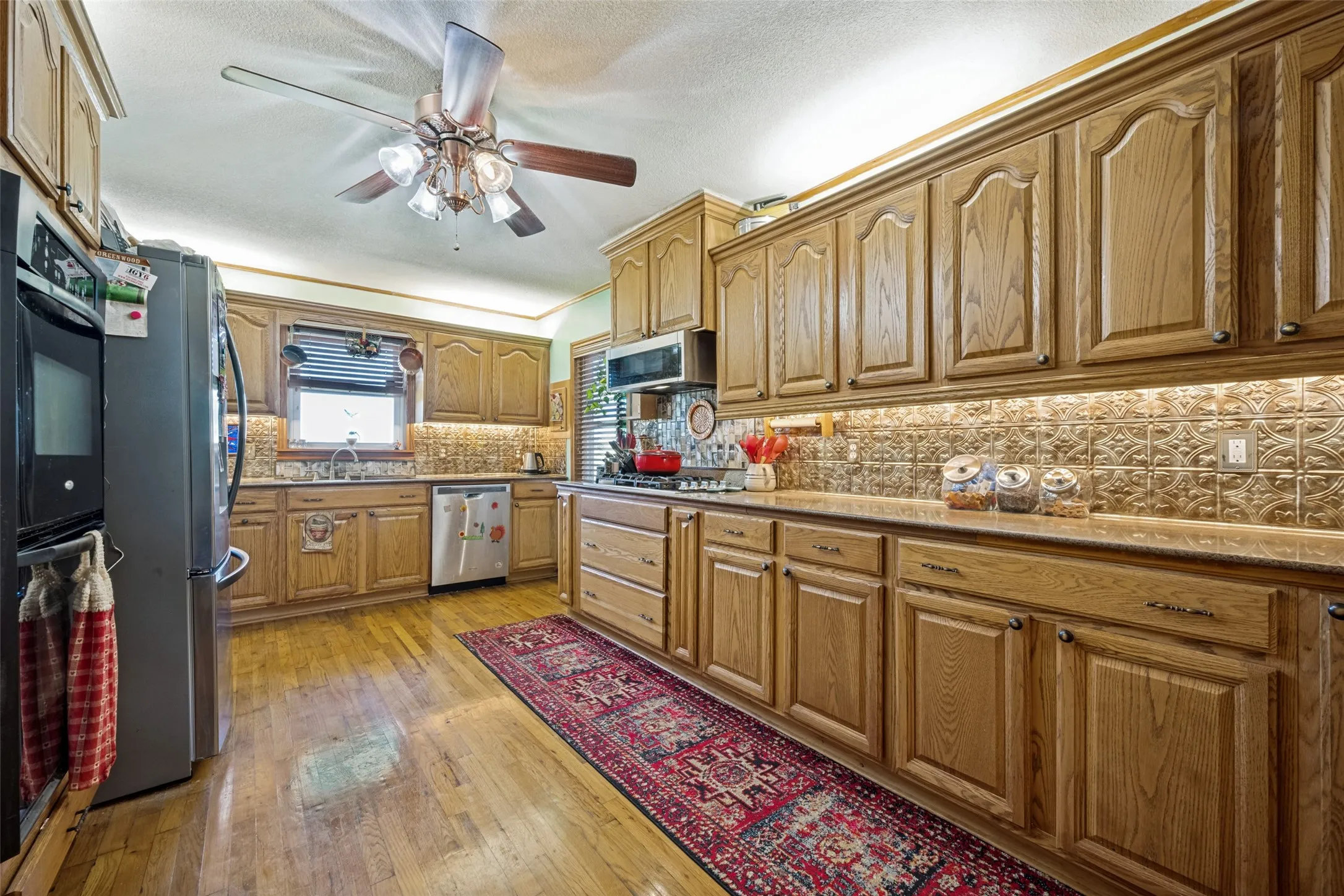 Extensive wood cabinetry, patterned tile backsplash, wood-finish flooring, and a ceiling fan with integrated lighting