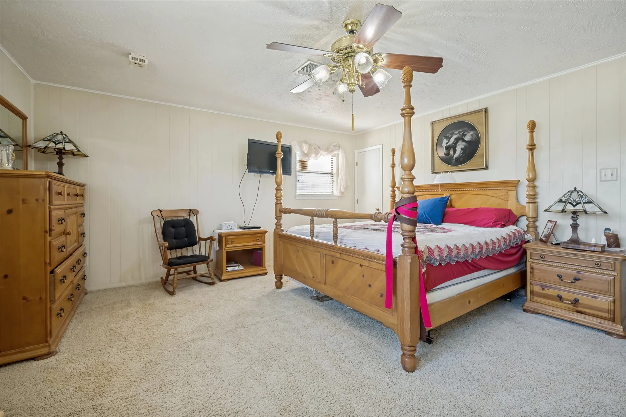 Plush carpeting, paneled walls, ceiling fan with integrated lighting, and a window with blinds