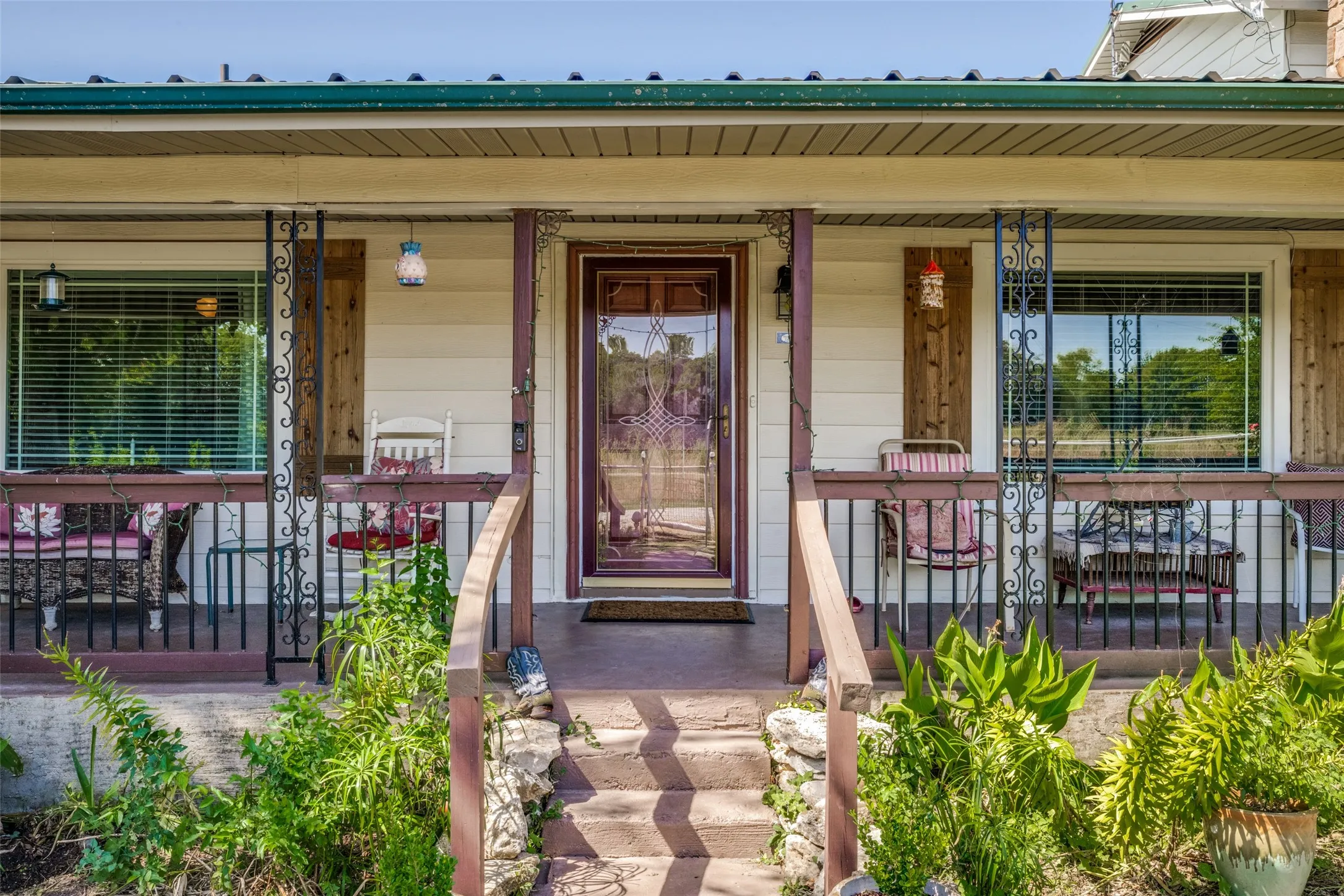 Covered front porch with decorative iron railings, wood-finish columns, and a paneled glass entry door