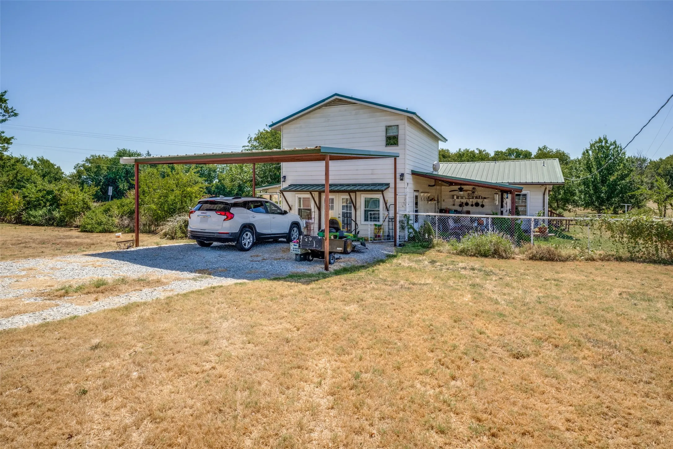 Two-story residence with a metal roof, an attached carport, and a gravel driveway