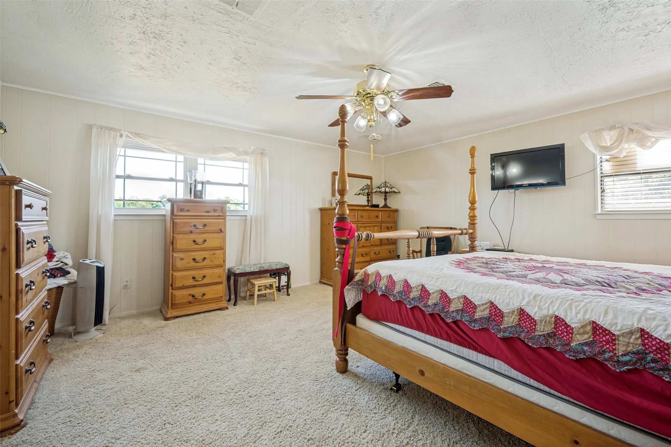 Carpeted flooring, paneled walls, windows with blinds and sheer curtains, and a ceiling fan with integrated lighting