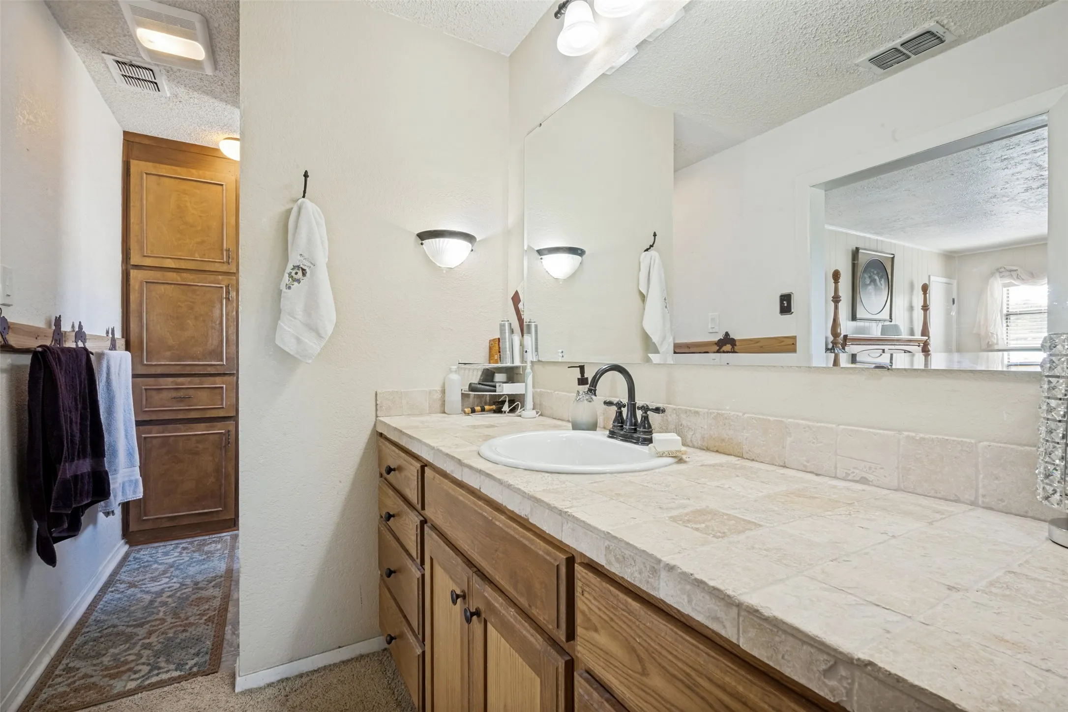 Vanity featuring a drop-in sink with a dark-finish faucet, tiled countertop, and wood-finish cabinetry