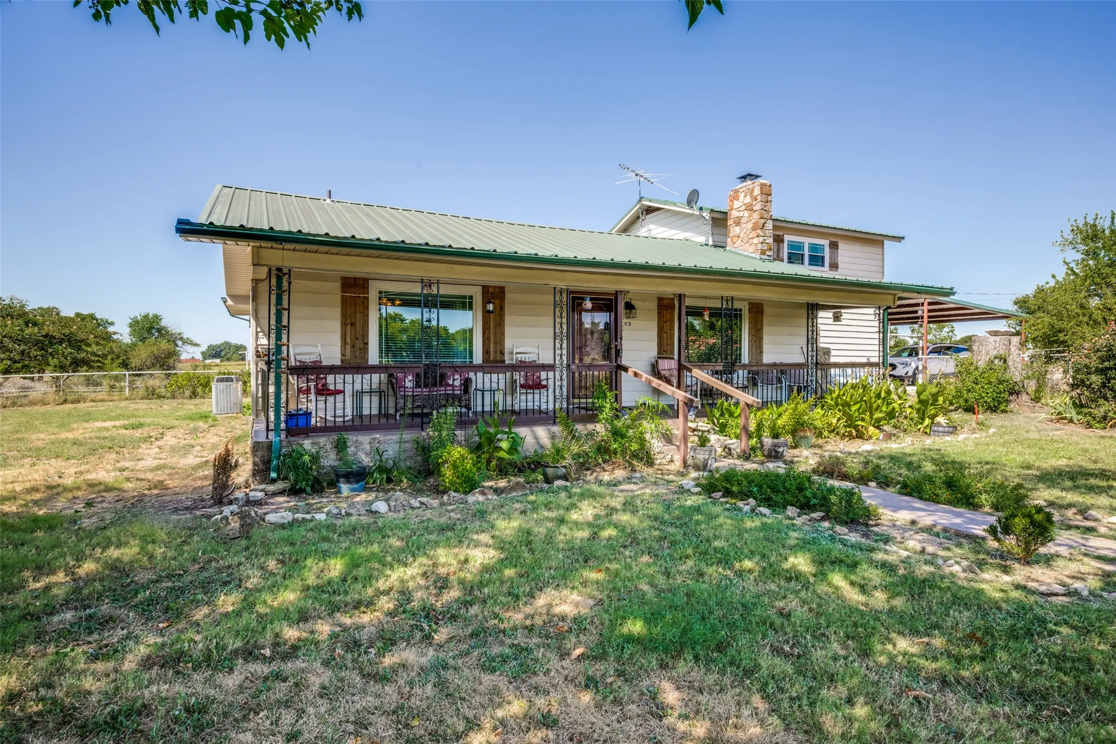 Property with a green metal roof, a stone-clad chimney, a covered front porch with railings, and a two-story elevation