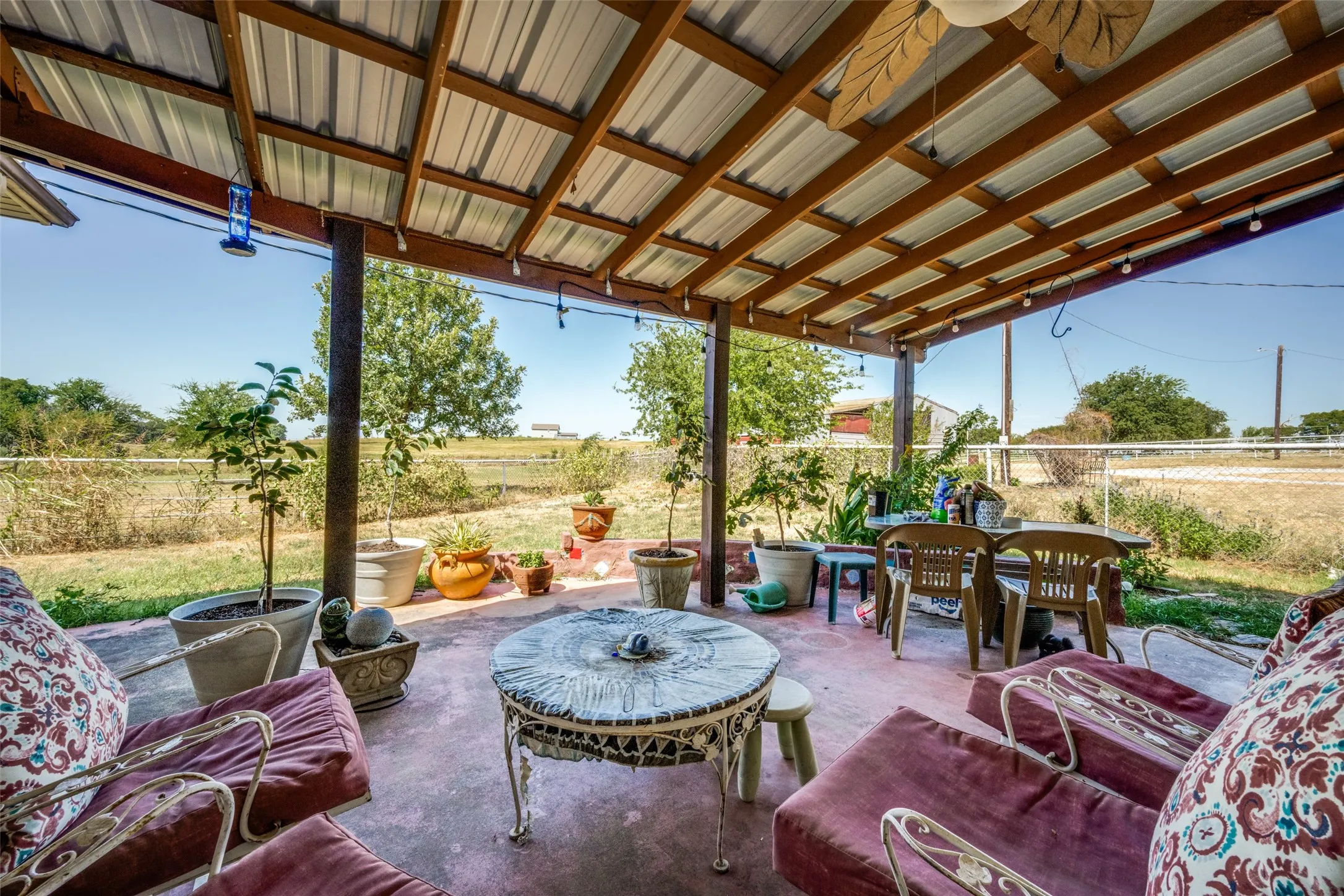 Covered back patio with a corrugated metal roof, exposed wood beams, and string lighting