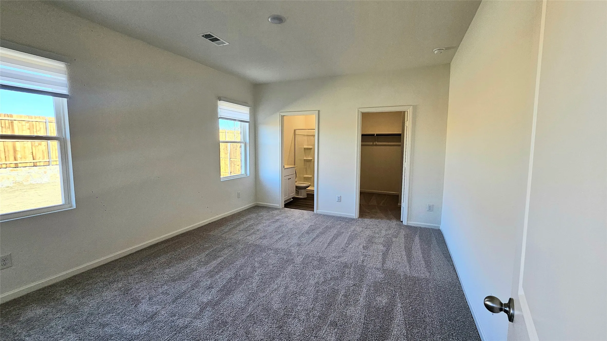 Carpeted interior with two windows, a built-in closet with shelving, and an en-suite bathroom featuring a vanity and shower-over-tub