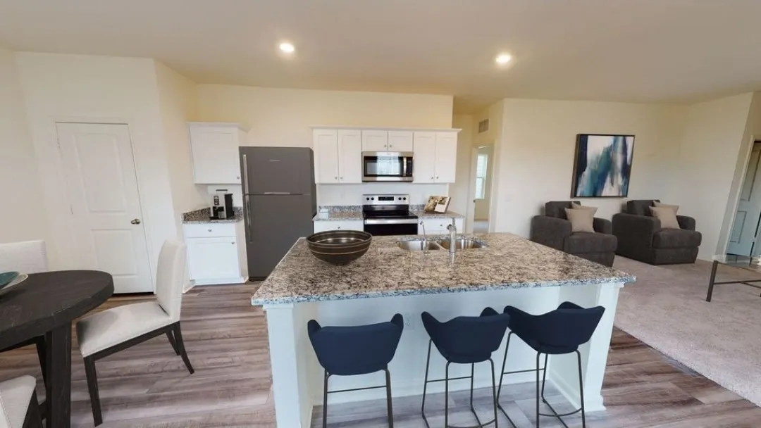 Kitchen featuring white cabinetry, stainless steel appliances, a center island with a double basin sink, and granite countertops