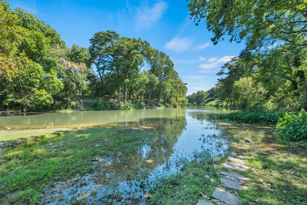 Expansive waterside property featuring a natural waterway, lush green foliage, and mature trees framing the shoreline