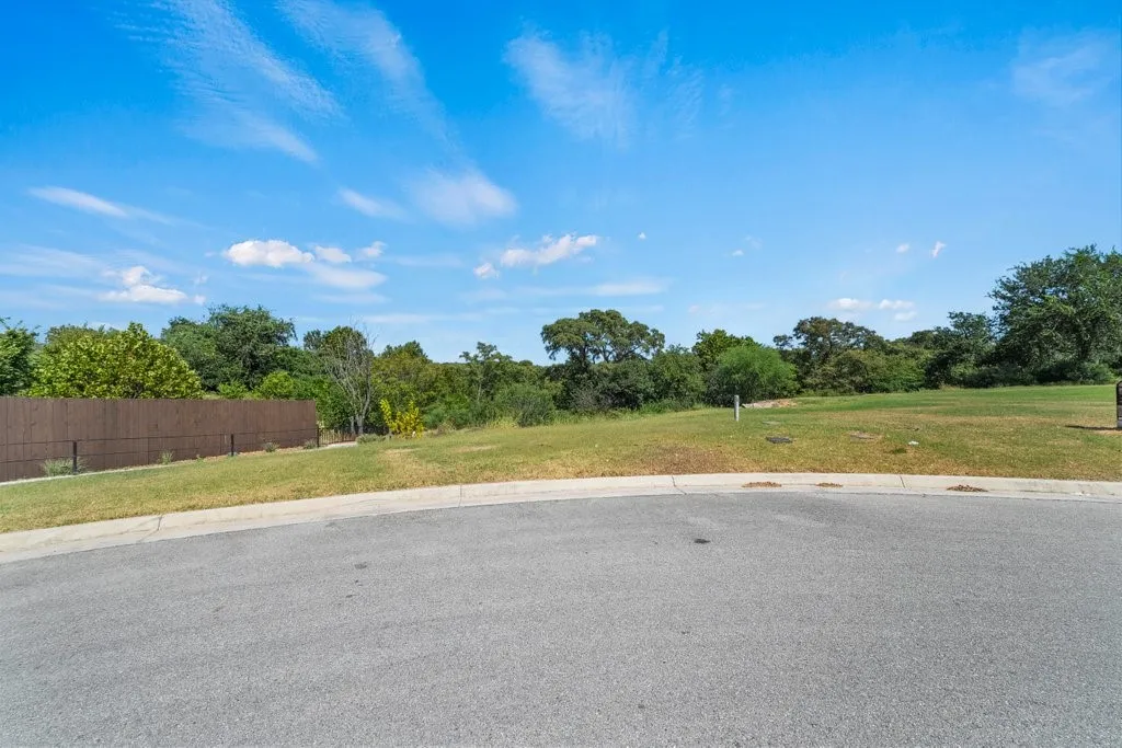 Expansive undeveloped lot featuring a manicured lawn, mature trees, and a privacy fence