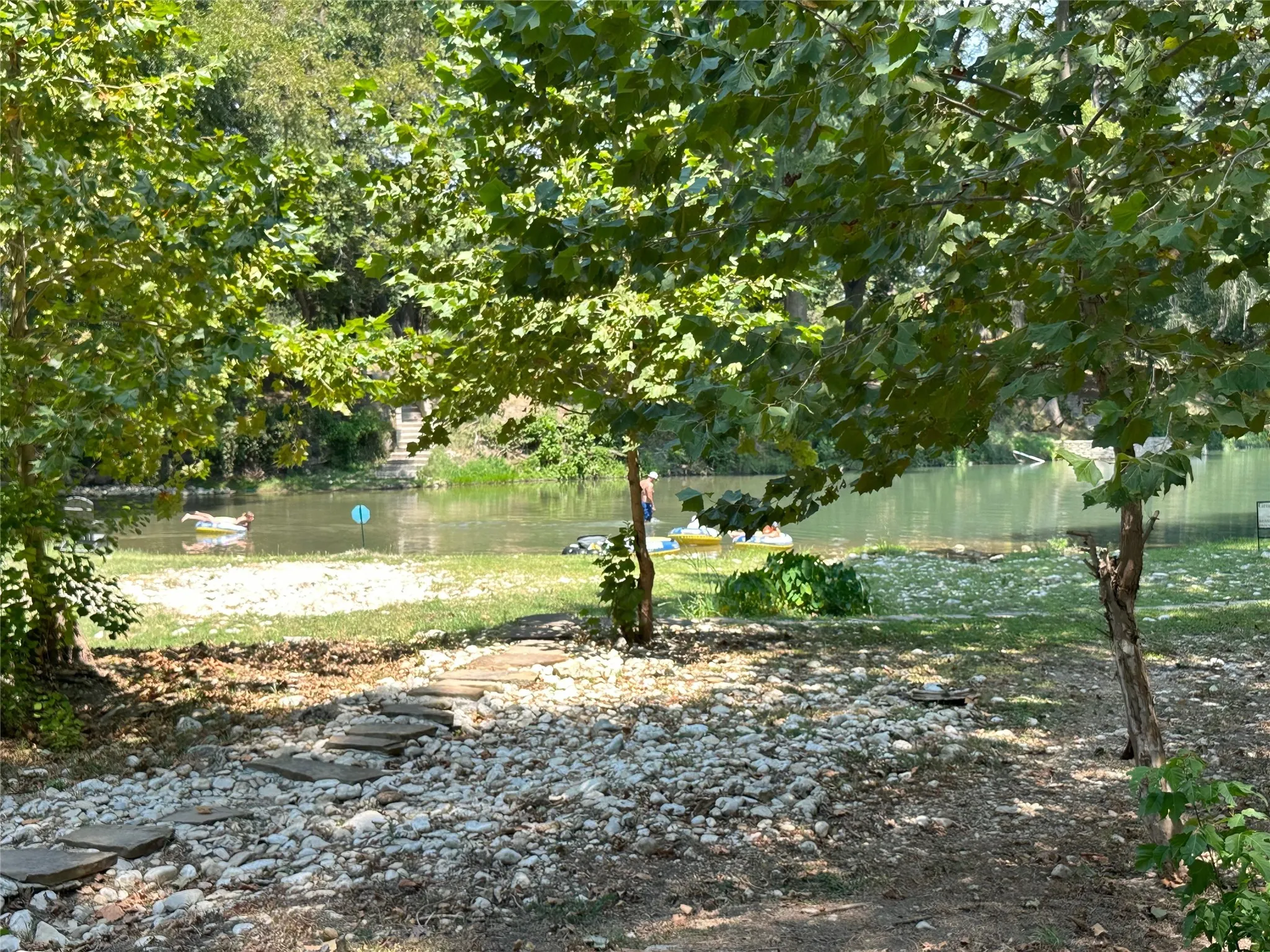 Mature trees providing shade, natural water feature, stone pathway, gravel hardscaping, and lush foliage