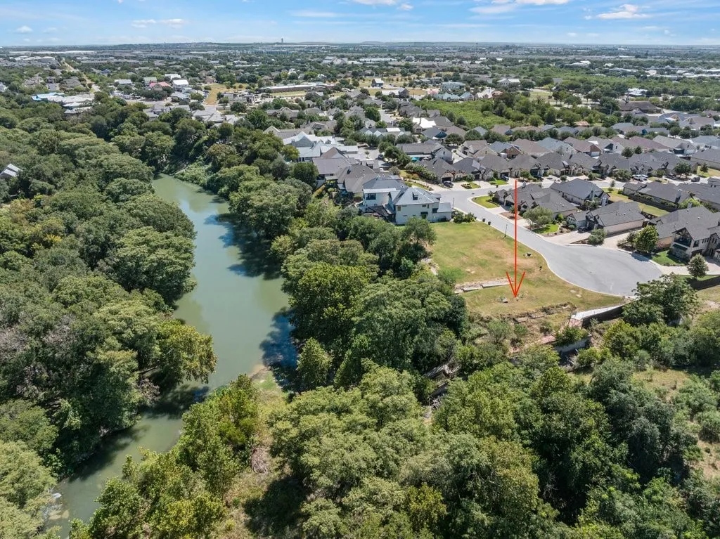 Cleared lot with a paved street frontage, surrounded by mature trees and a natural waterway