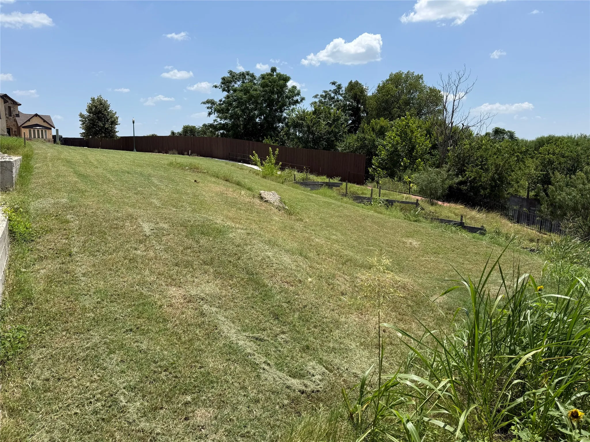 Expansive grassy area with a partial privacy fence and mature trees