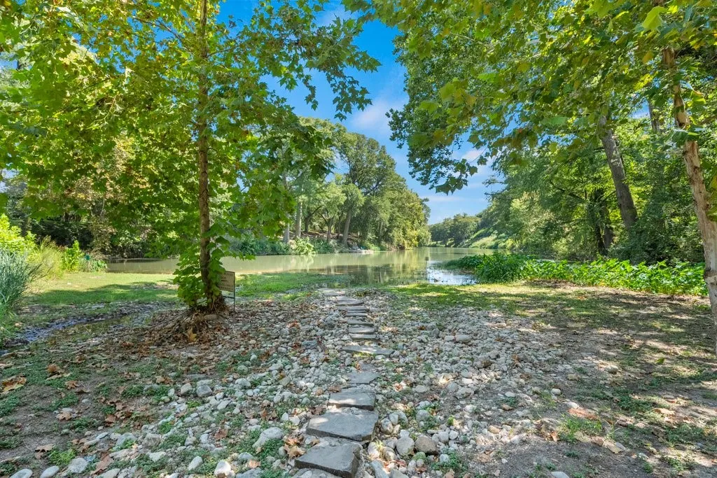 Waterfront property featuring a stone pathway, mature trees, and natural landscaping