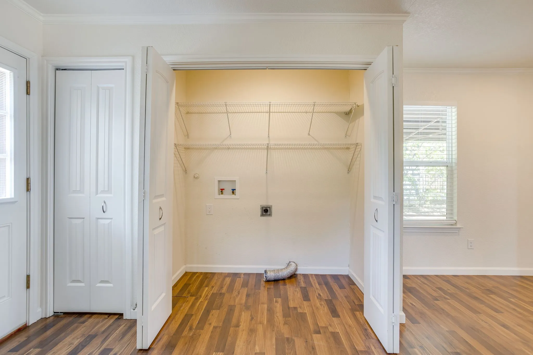 Laundry closet with wire shelving, washer and dryer hookups, and wood laminate flooring