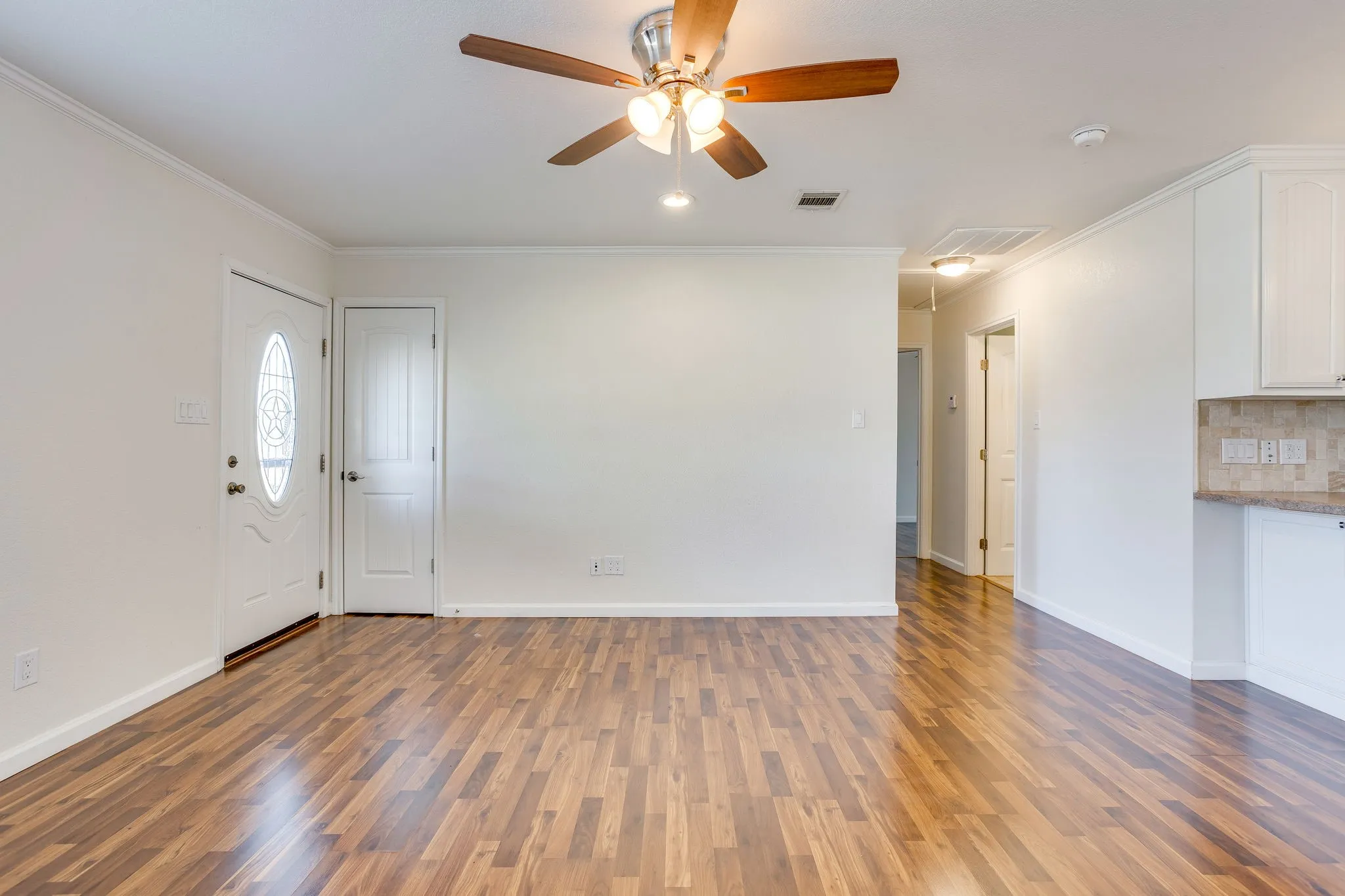 wood laminate flooring with ample wall space, crown molding and a ceiling fan