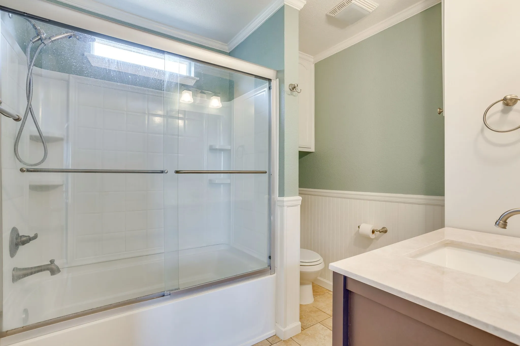Built-in tub/shower combination with glass enclosure, single vanity with integrated sink, beadboard wainscoting, and tile flooring
