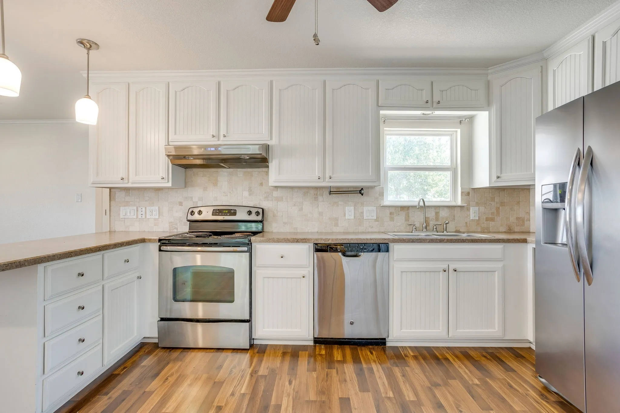 Kitchen featuring white cabinetry, stainless steel appliances, a tiled backsplash, wood laminate flooring, and pendant lighting