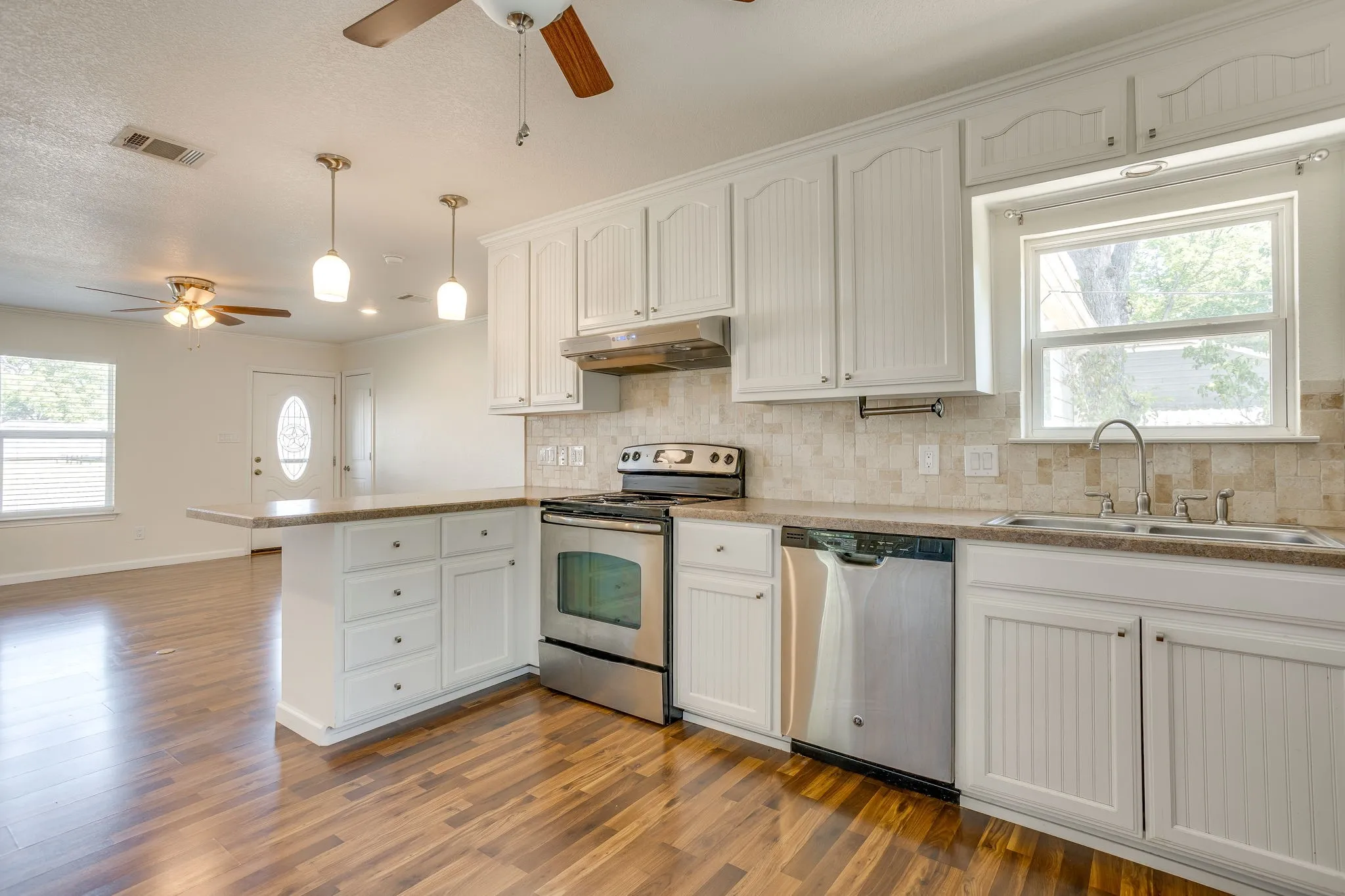 White cabinetry, stainless steel appliances, breakfast bar, tile backsplash, and wood laminate flooring