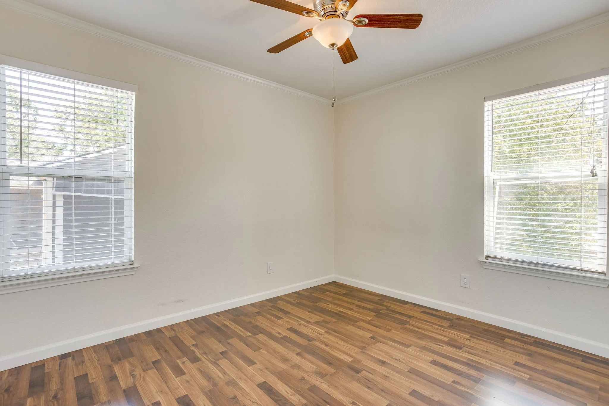 Wood laminate flooring throughout, two windows with blinds, and a ceiling fan with light fixture