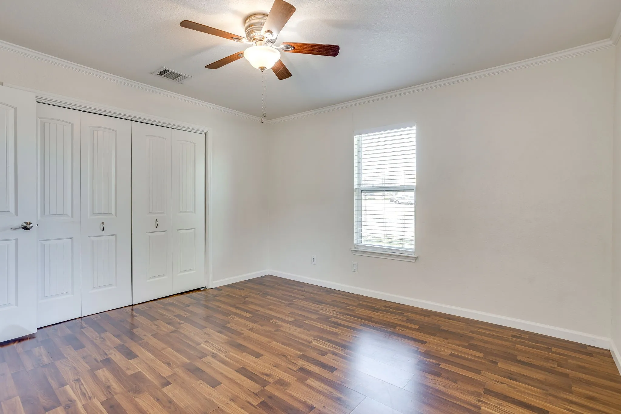 Wood laminate flooring, white paneled bifold closet doors, white paneled door, ceiling fan with integrated lighting, and a window with blinds