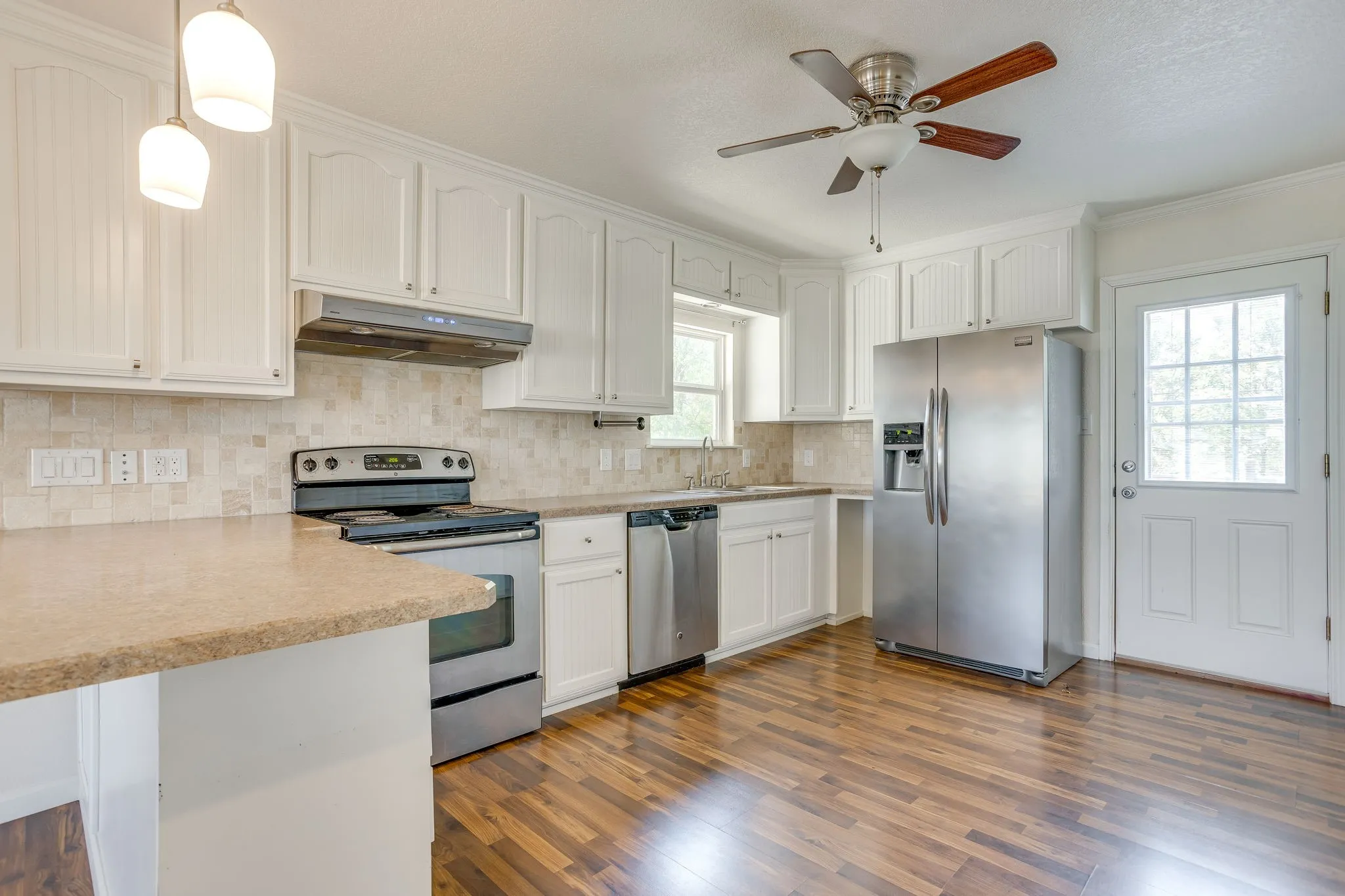 Kitchen featuring wood laminate flooring, white cabinetry, stainless steel appliances, a ceiling fan, and a glass-paneled exterior door