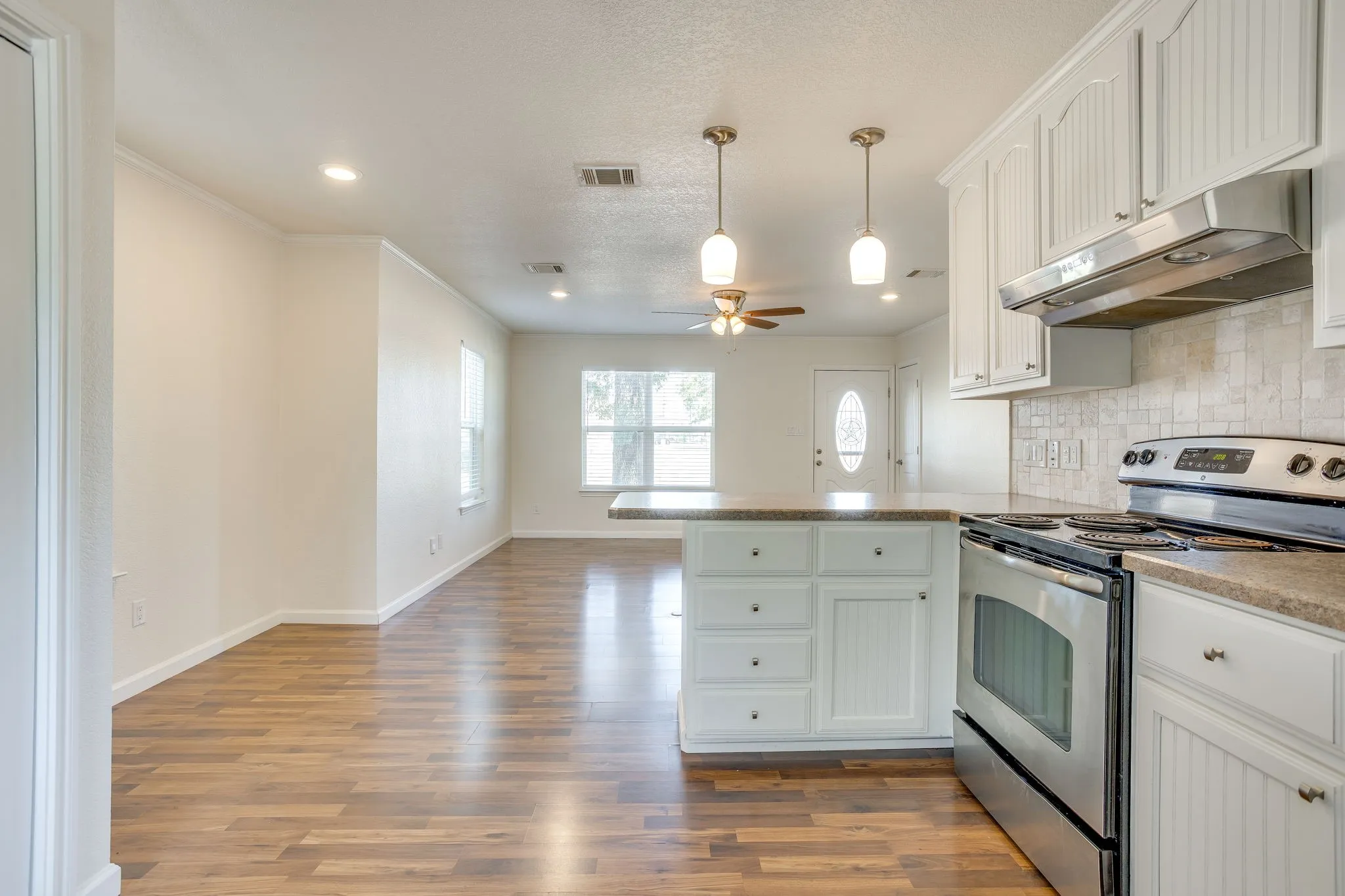 Modern kitchen featuring white cabinetry with hardware accents, stainless steel appliances including a gas range and hood, wood laminate flooring throughout, quartz countertops, and recessed and pendant lighting