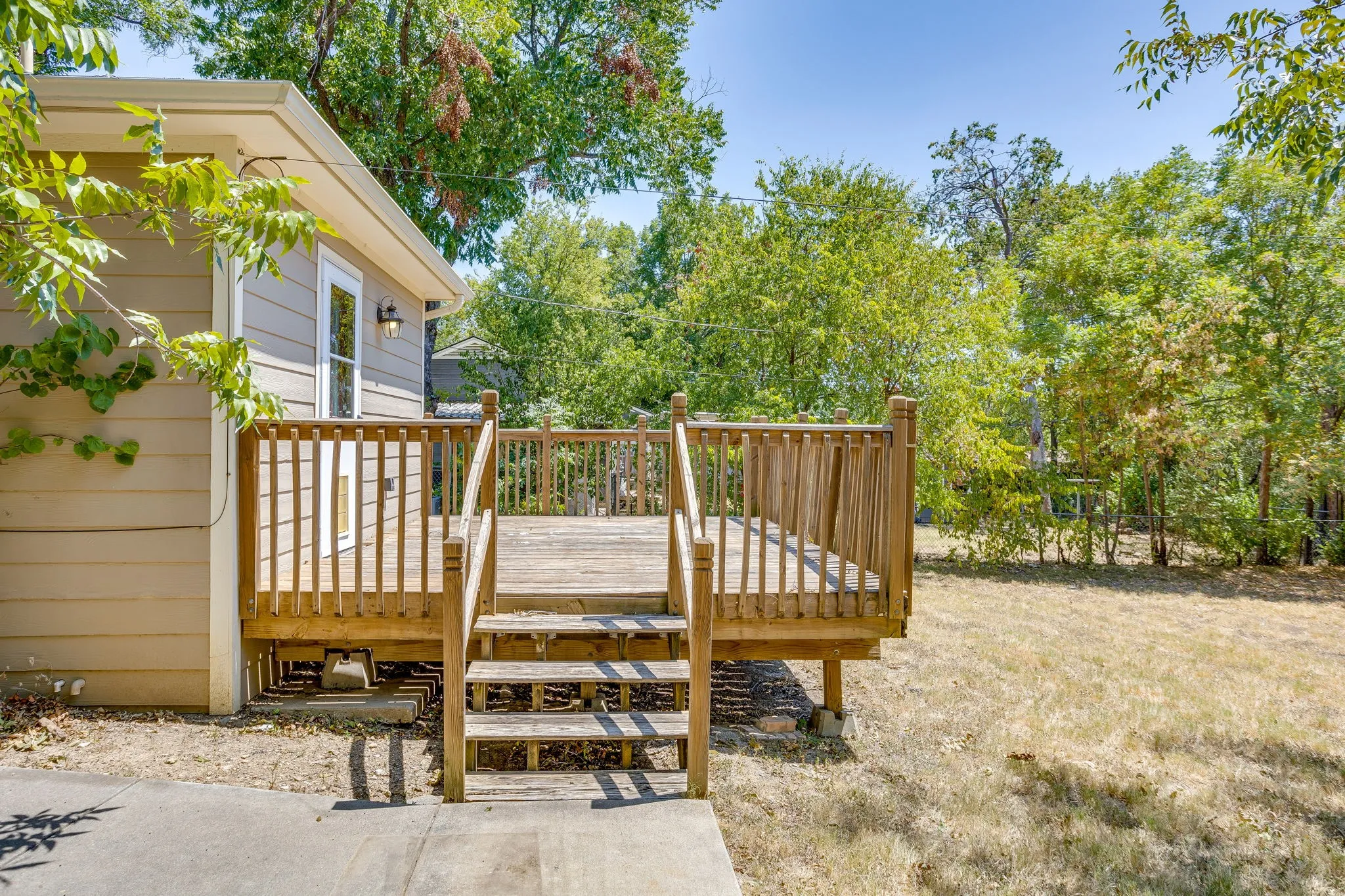Expansive wooden deck with railing, stairs, exterior siding, outdoor lighting fixture, and a glass-paneled door