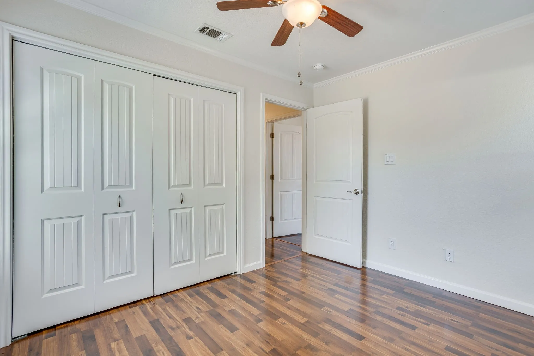 Spacious primary bedroom showcasing wood laminate flooring, dual closets with six-panel doors, ceiling fan with integrated lighting, and direct access to an ensuite bathroom