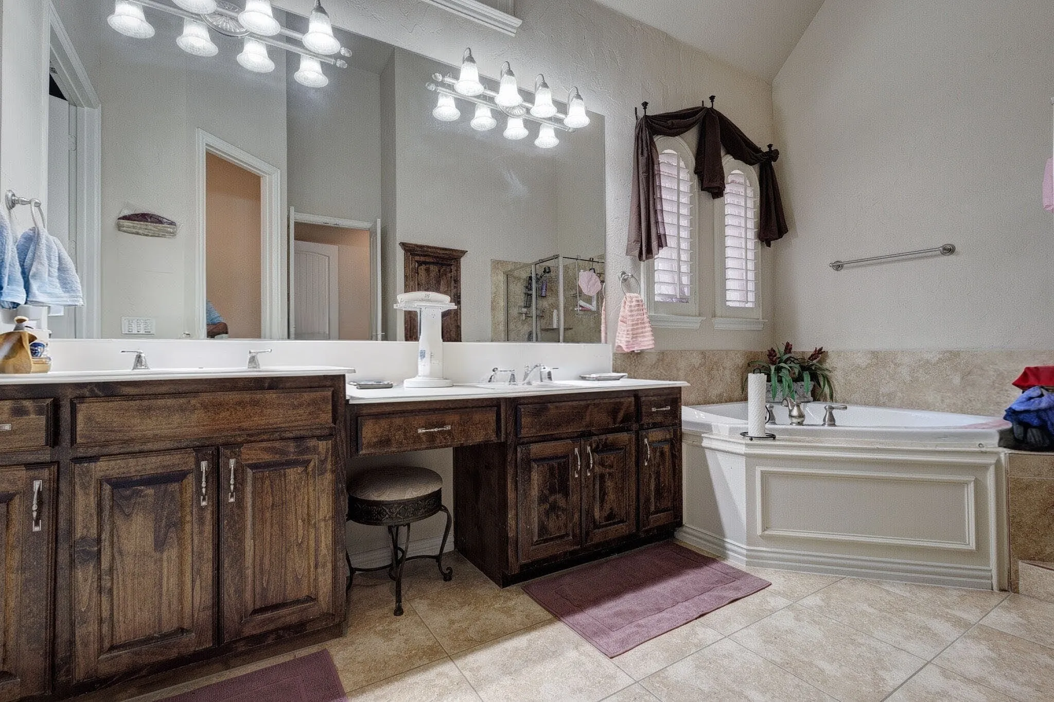 Dual vanity with integrated sinks, dark wood-finish cabinetry, built-in soaking tub, and shuttered windows