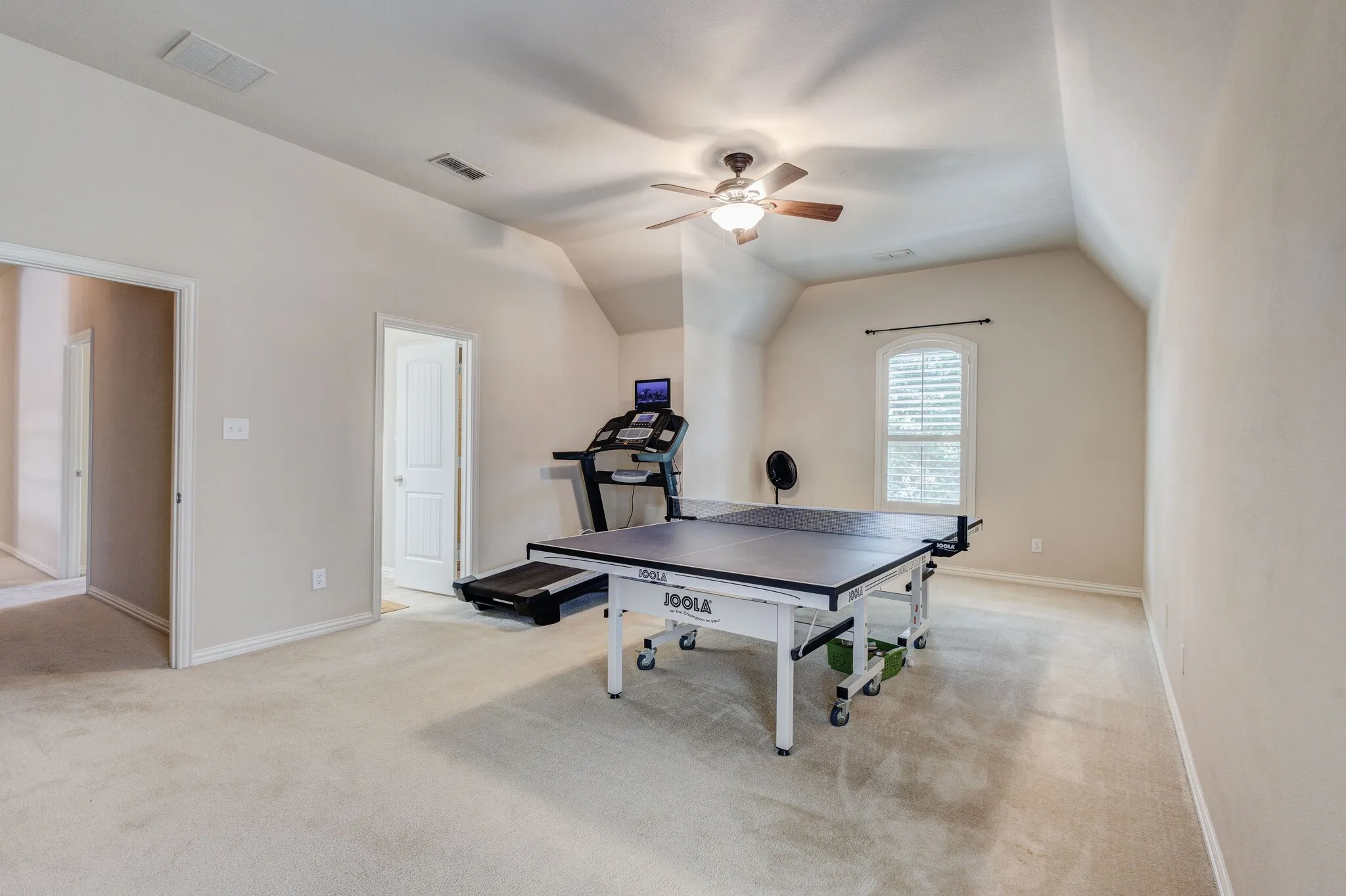 Carpeted room with a vaulted ceiling, ceiling fan with light fixture, and arched window with white louvered​​‌​​​​‌​​‌‌​‌‌​​​‌‌​‌​‌​‌​​​‌​​ blinds