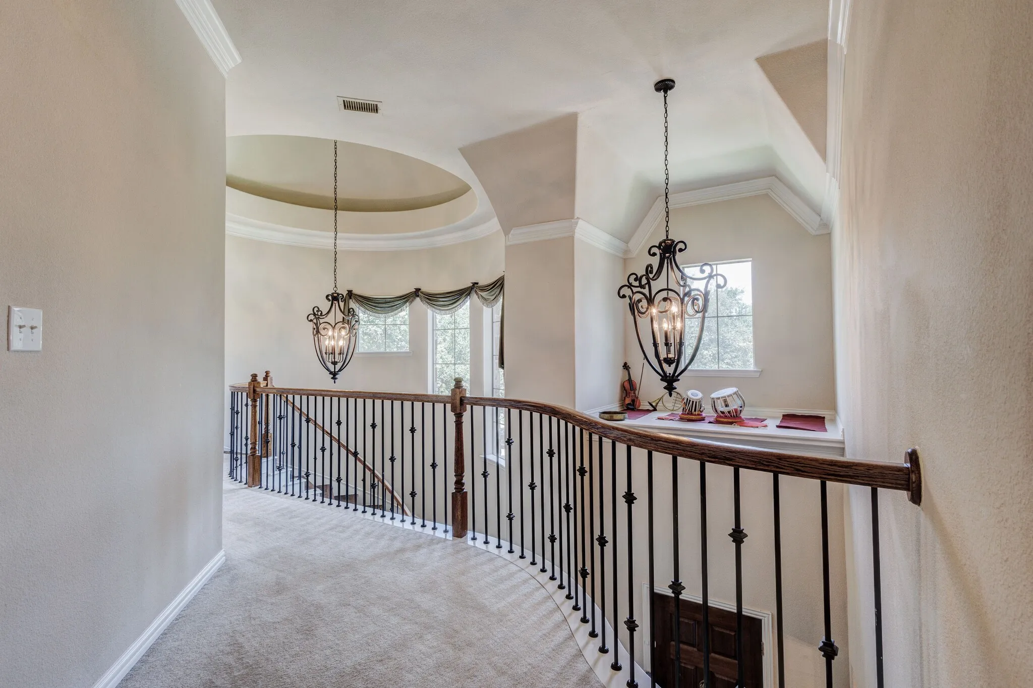Curved hallway with iron baluster railing, wood handrail, recessed dome ceiling, and decorative pendant lighting
