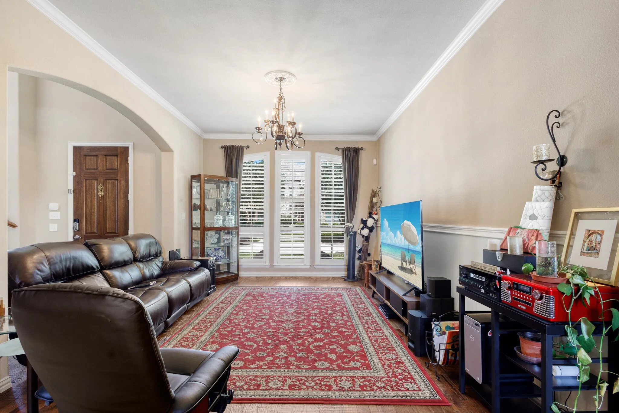 Archway entry, crown molding, chandelier lighting, wood-finish flooring, and window shutters