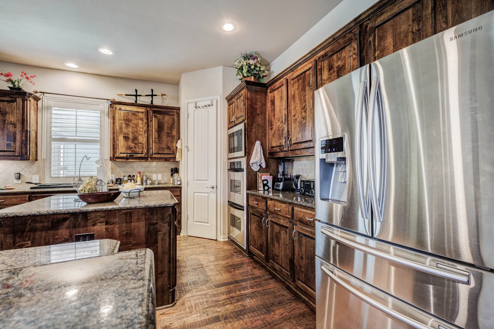 Stainless steel French door refrigerator, wood-finish cabinetry, granite countertops, wood-finish flooring, and recessed lighting
